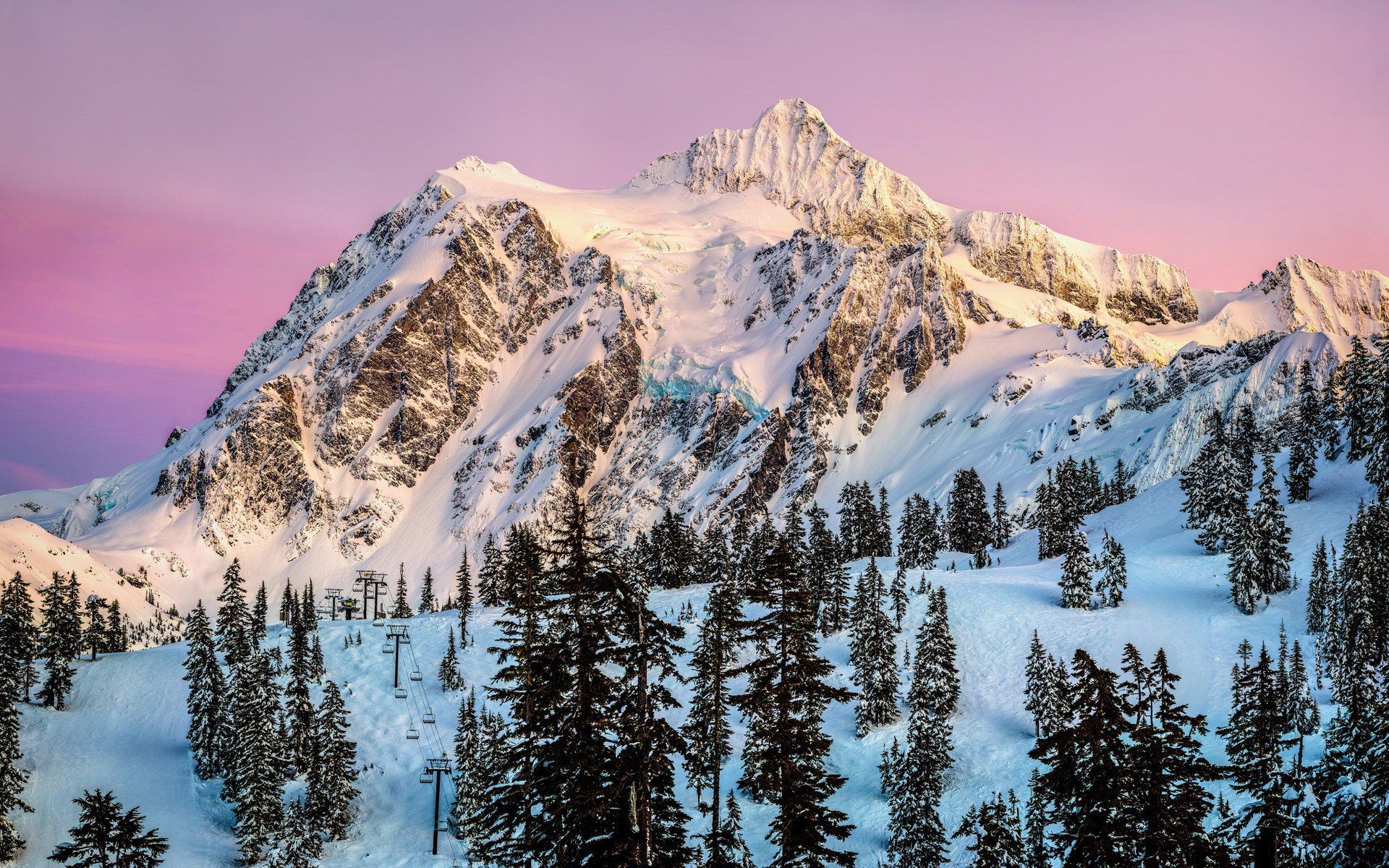 Snowy mountain peak with ski lift and pine trees at sunset HD Wallpaper