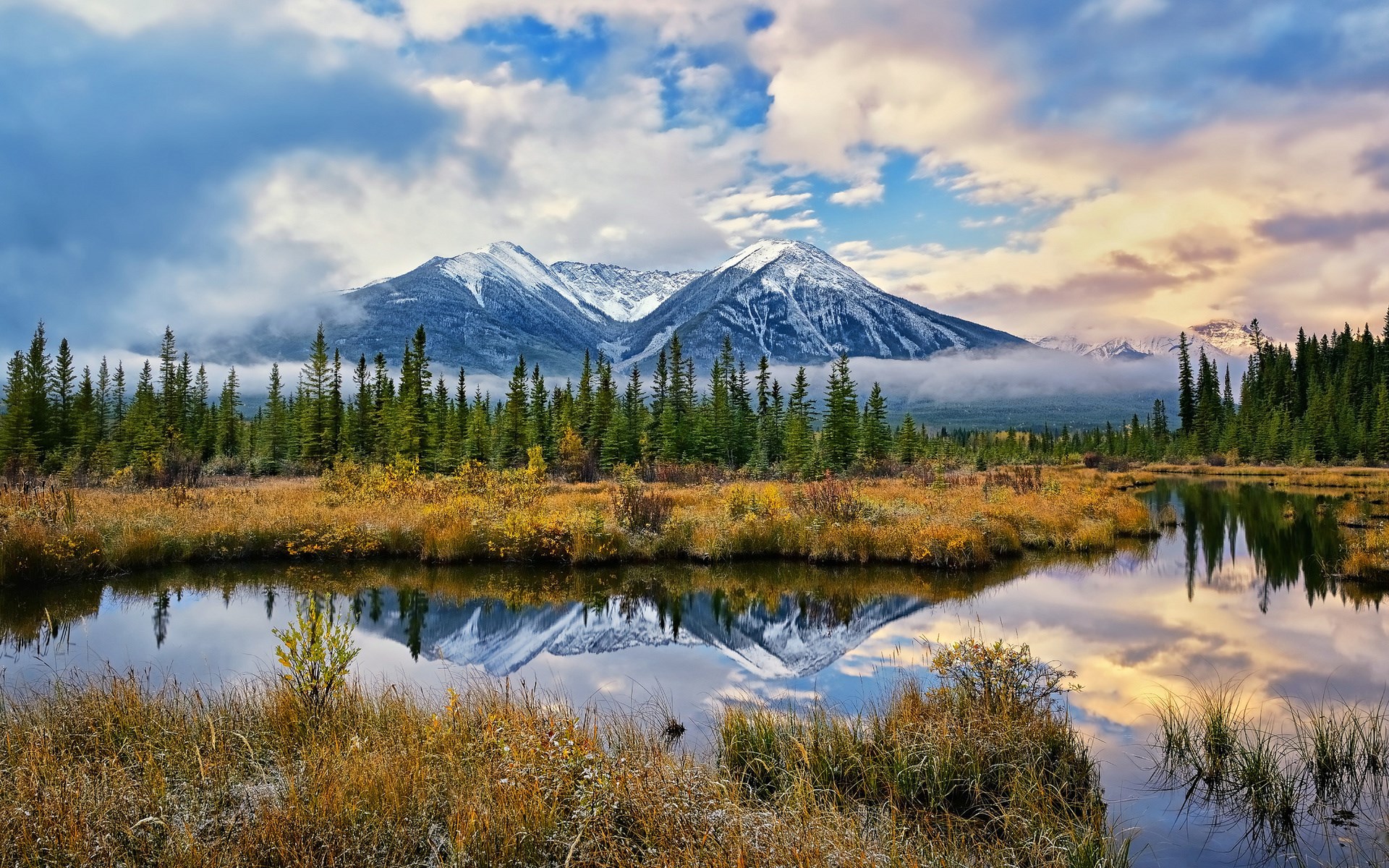 Snow-capped mountains reflected in a calm lake with evergreen trees HD Wallpaper