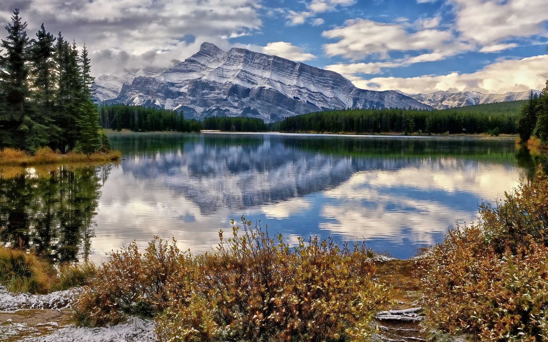 Snow-capped mountain reflected in a calm lake with pine trees HD Wallpaper