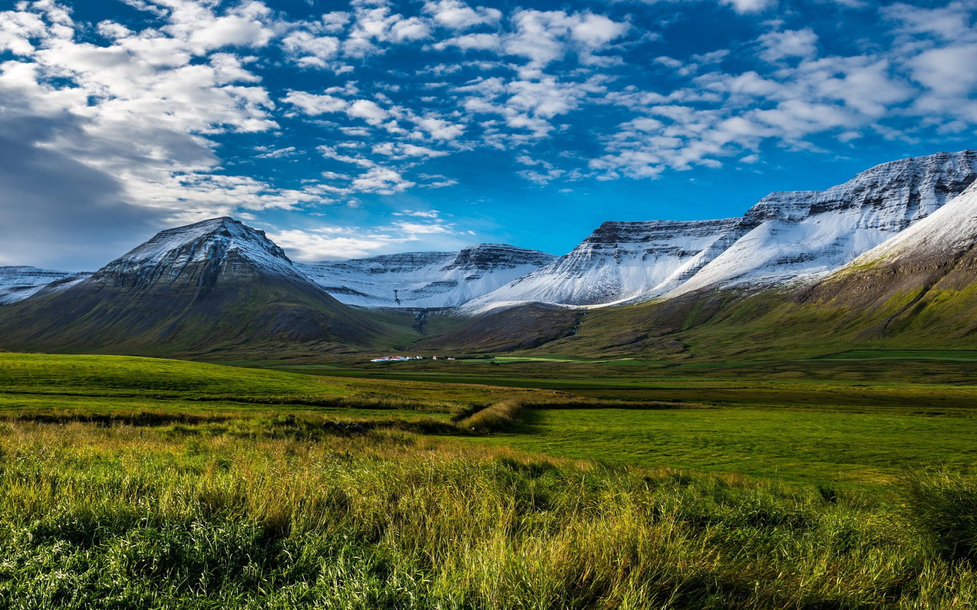 Snow-capped mountains and green fields under a cloudy sky HD Wallpaper