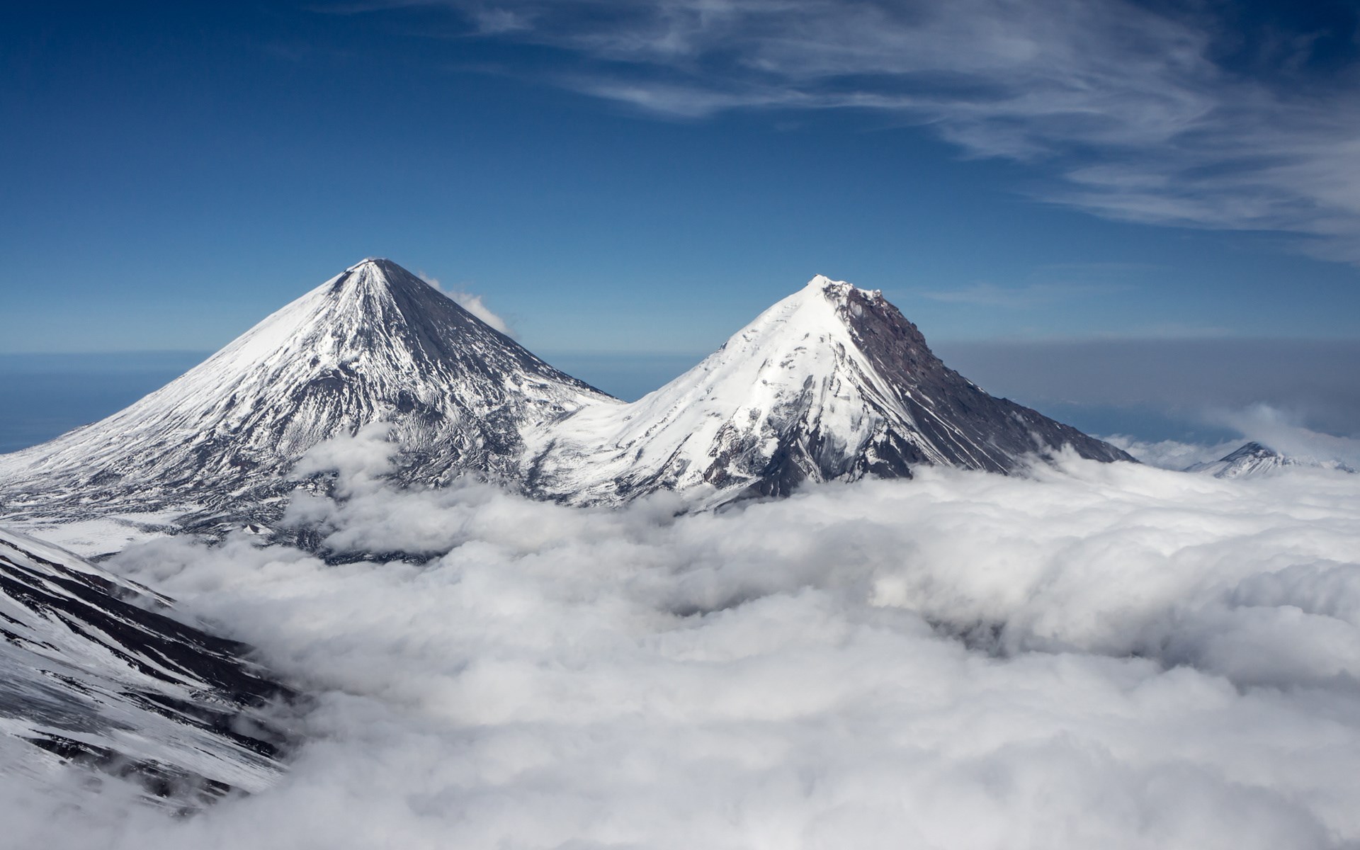 Snow-capped volcanoes above clouds under a blue sky HD Wallpaper