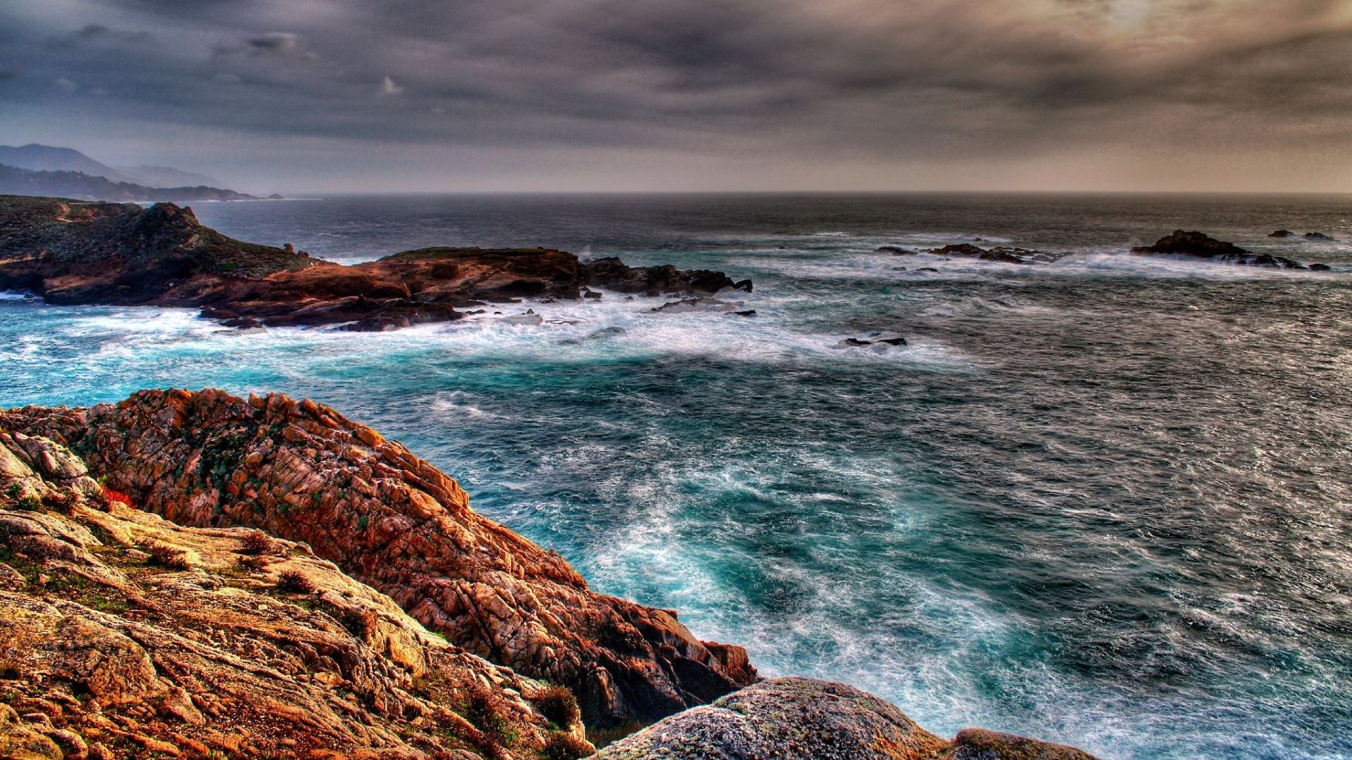 Rocky coastline with crashing waves under a cloudy sky HD Wallpaper