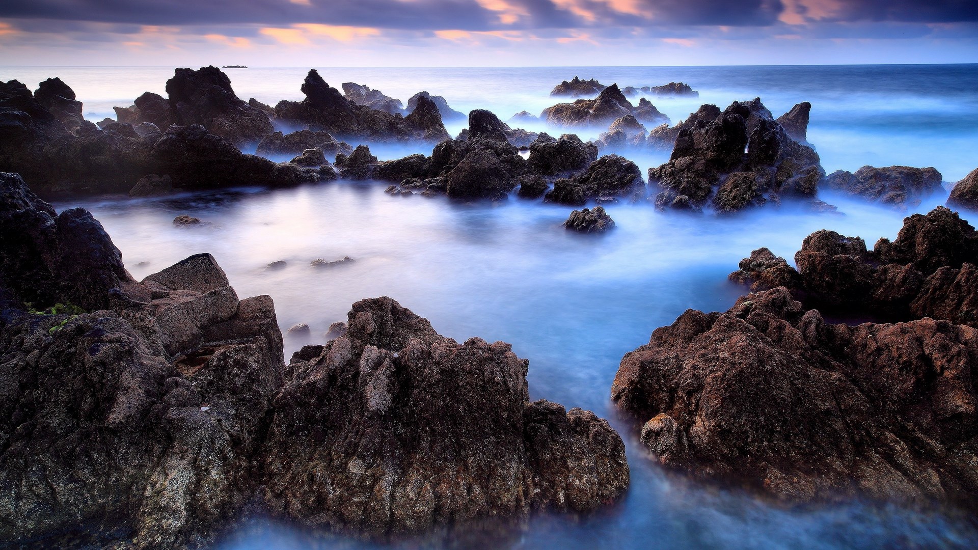 Rocky coastline with misty ocean waves at dusk HD Wallpaper