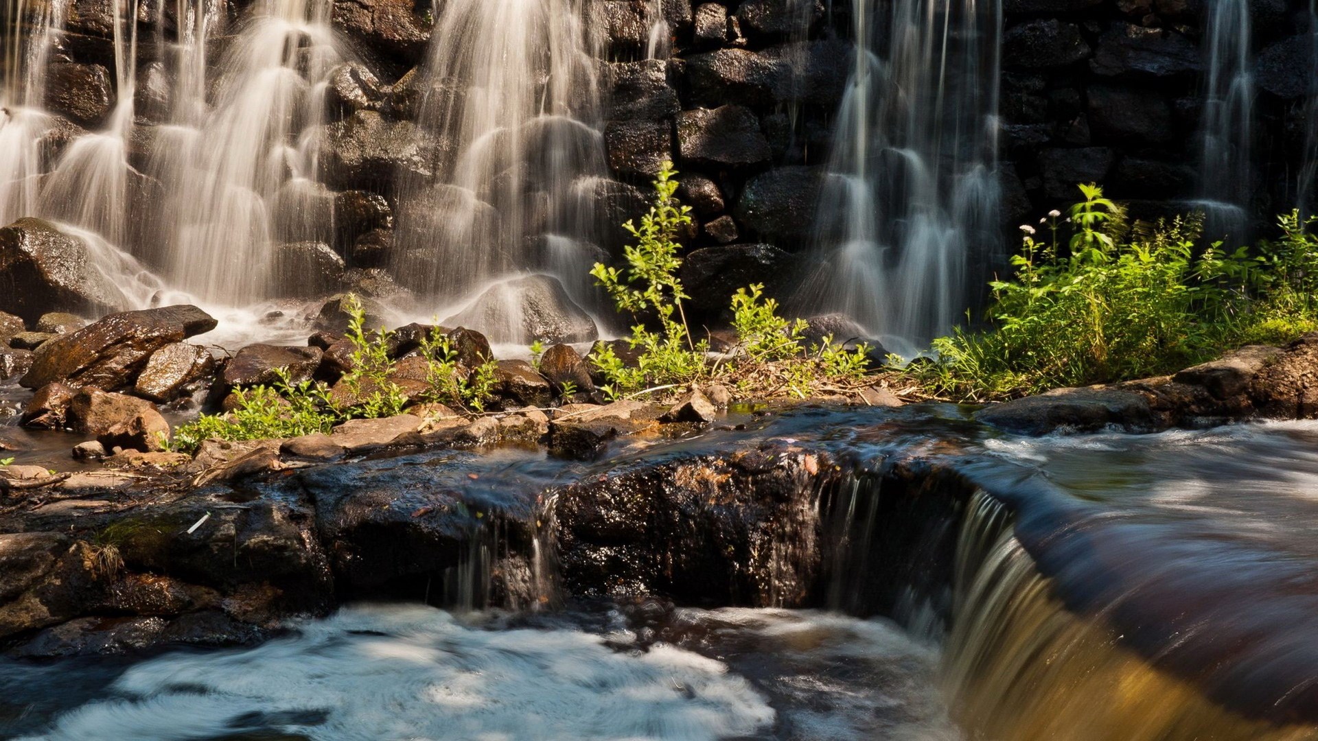 Waterfall cascading over rocks with green plants HD Wallpaper