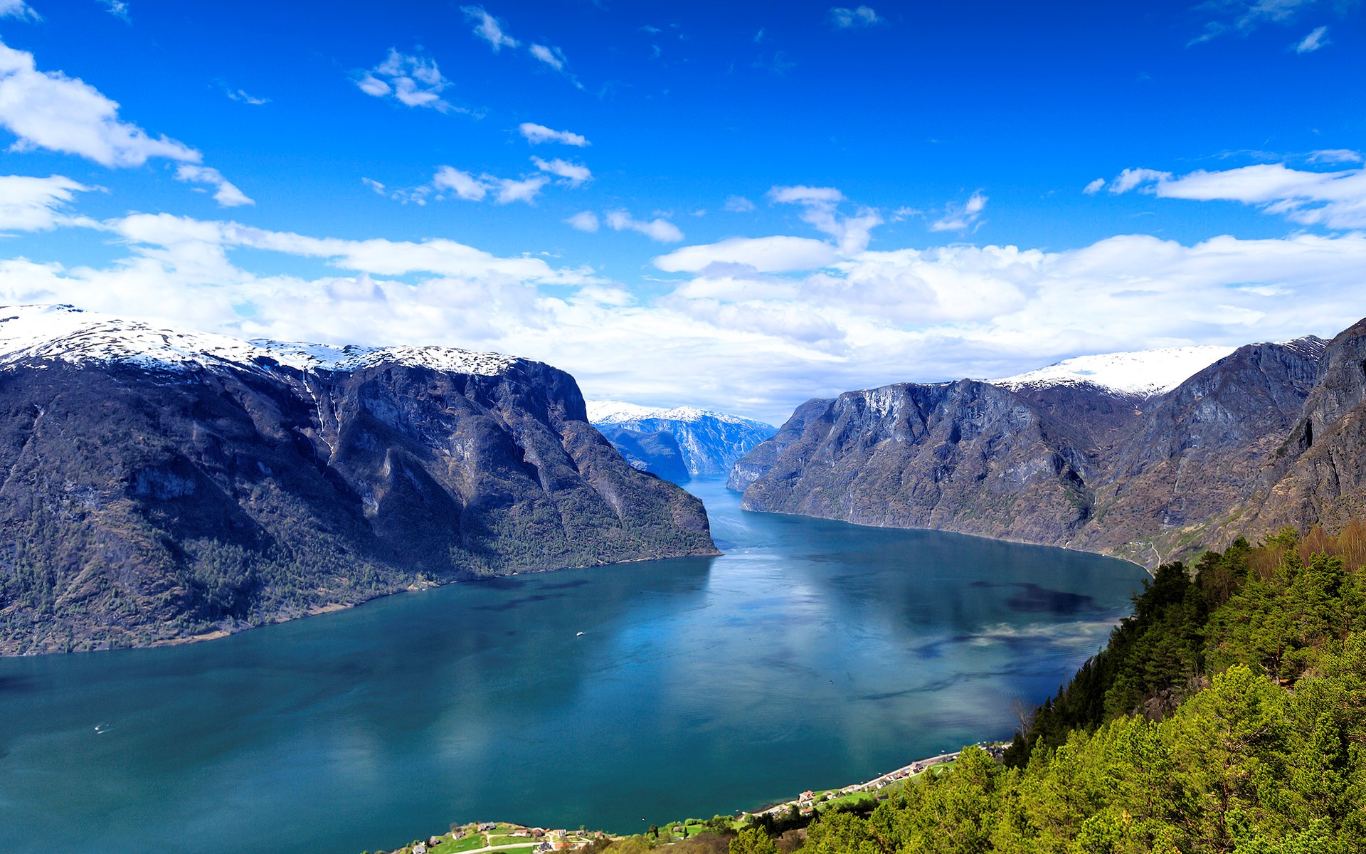A wide fjord with steep, snow-capped mountains under a blue sky. HD Wallpaper