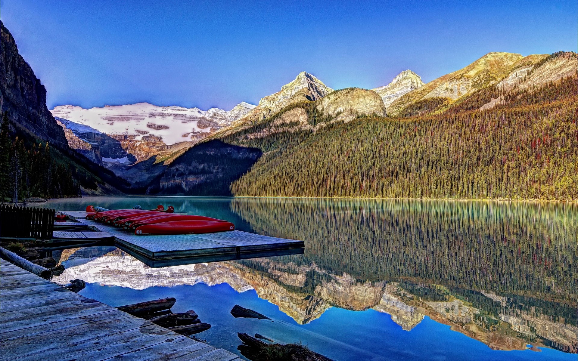 Red canoes on a dock at Lake Louise with mountains HD Wallpaper