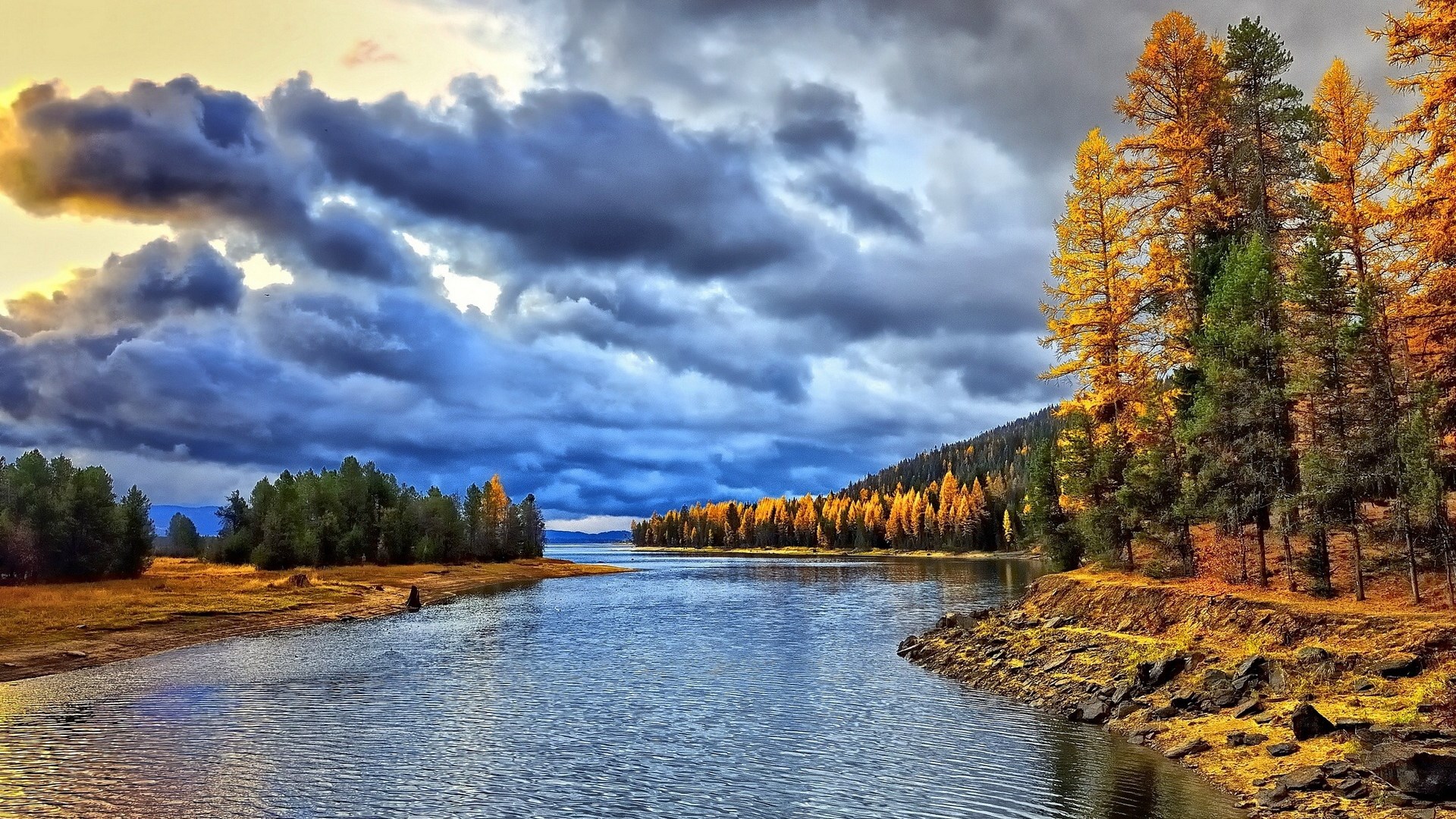 Autumn trees line a lake under stormy clouds HD Wallpaper