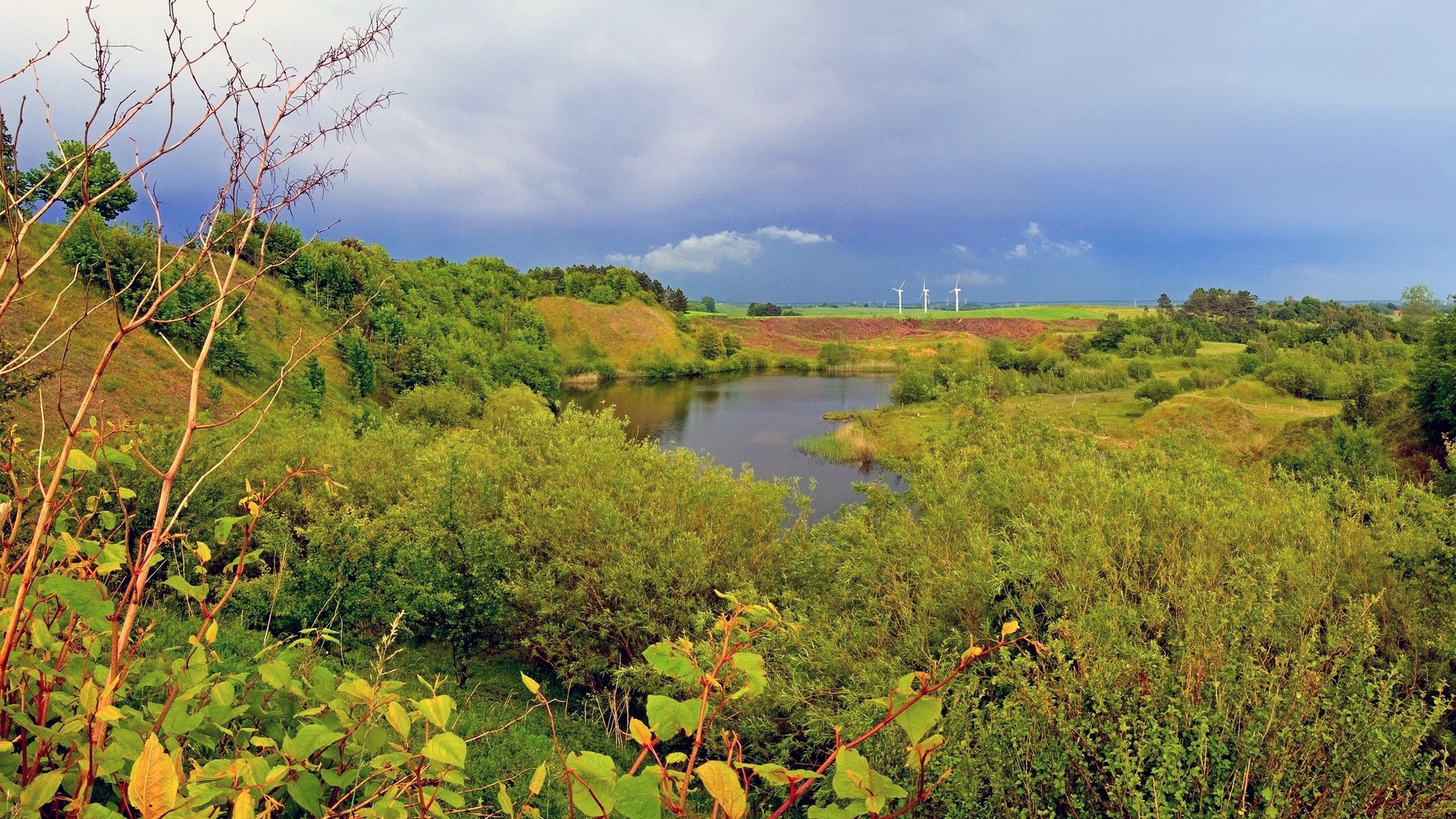 Wind turbines in a rural landscape with a lake HD Wallpaper