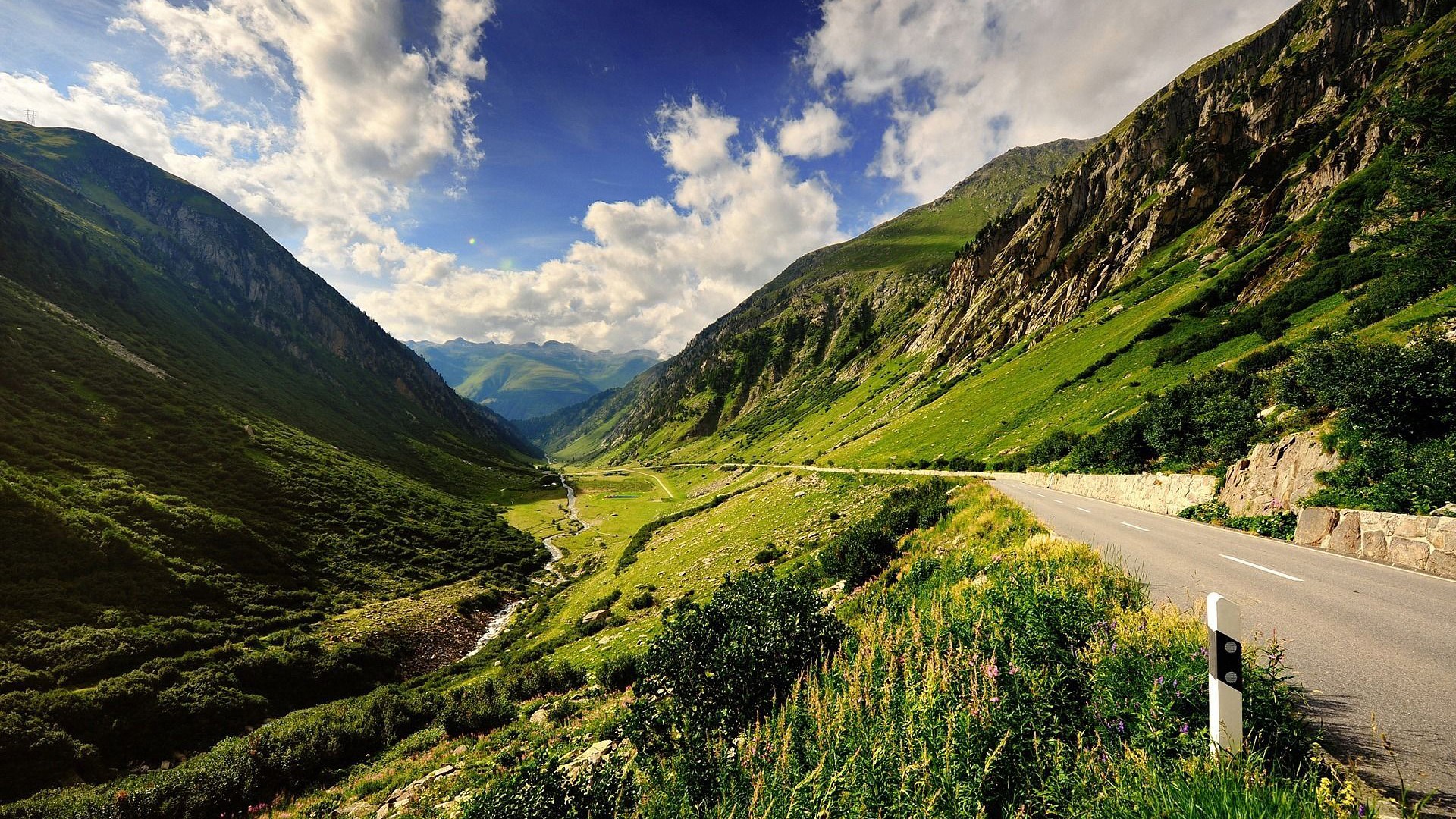 Mountain valley with a road and a stream HD Wallpaper