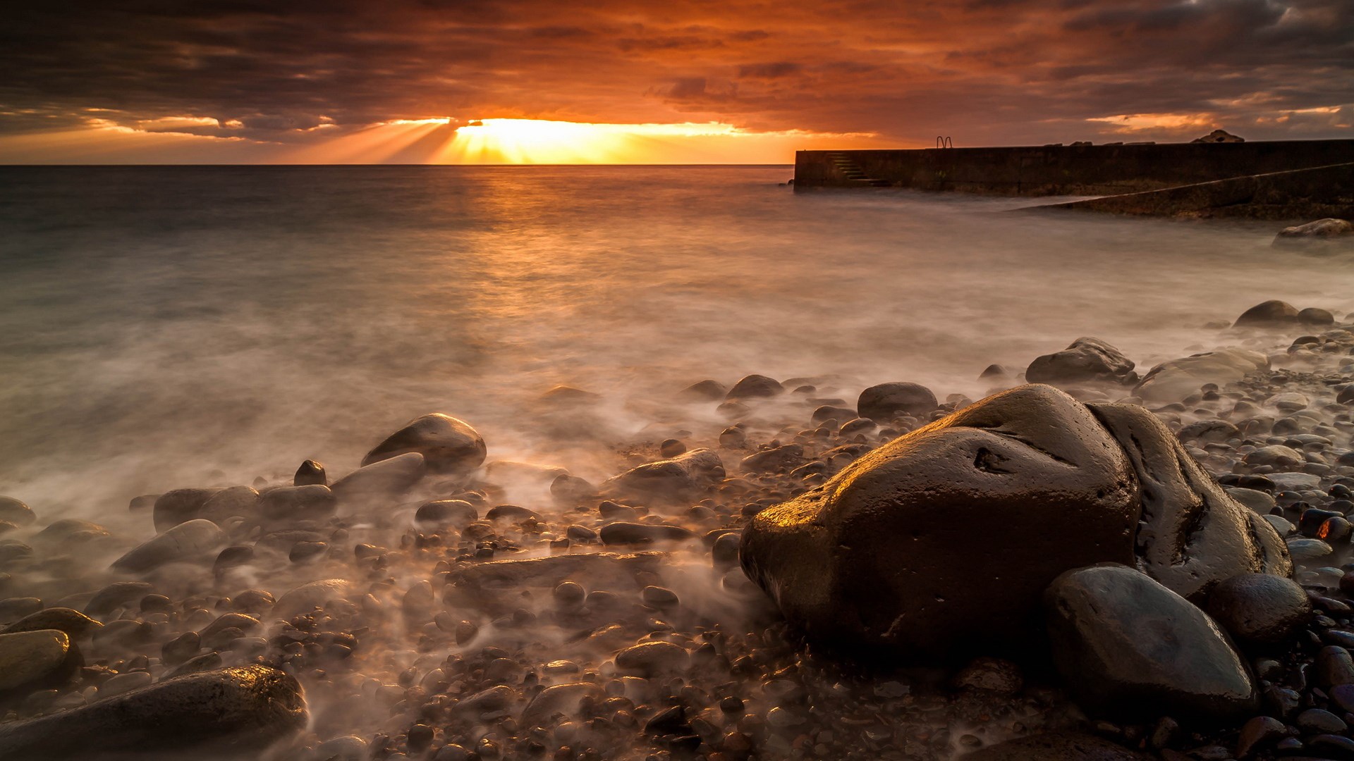 Sunset over rocky beach with pier HD Wallpaper