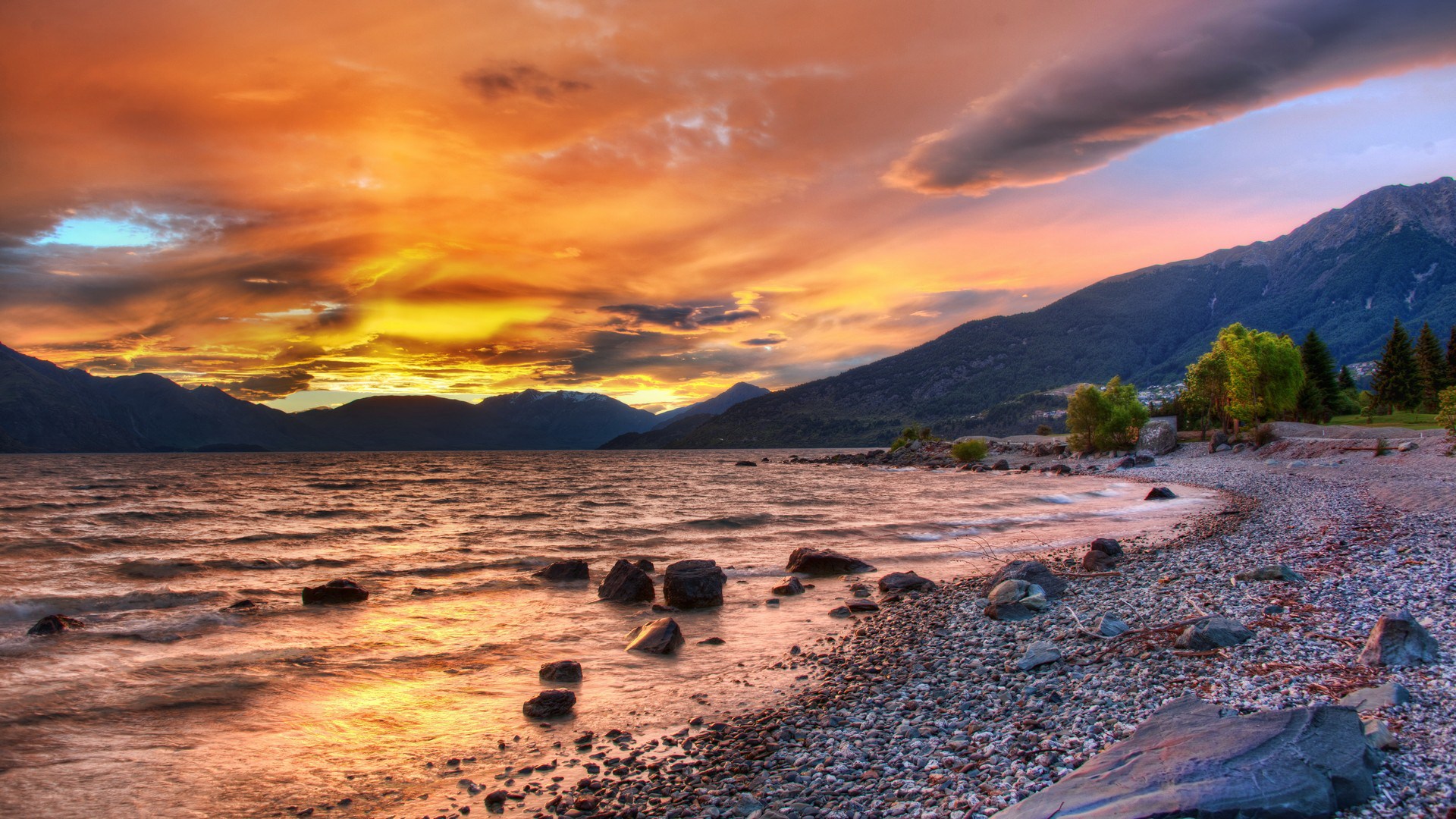 Sunset over a rocky lake shore with mountains HD Wallpaper