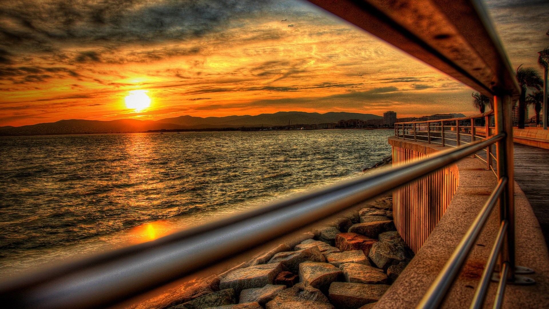 Sunset over the ocean with a boardwalk and railing HD Wallpaper