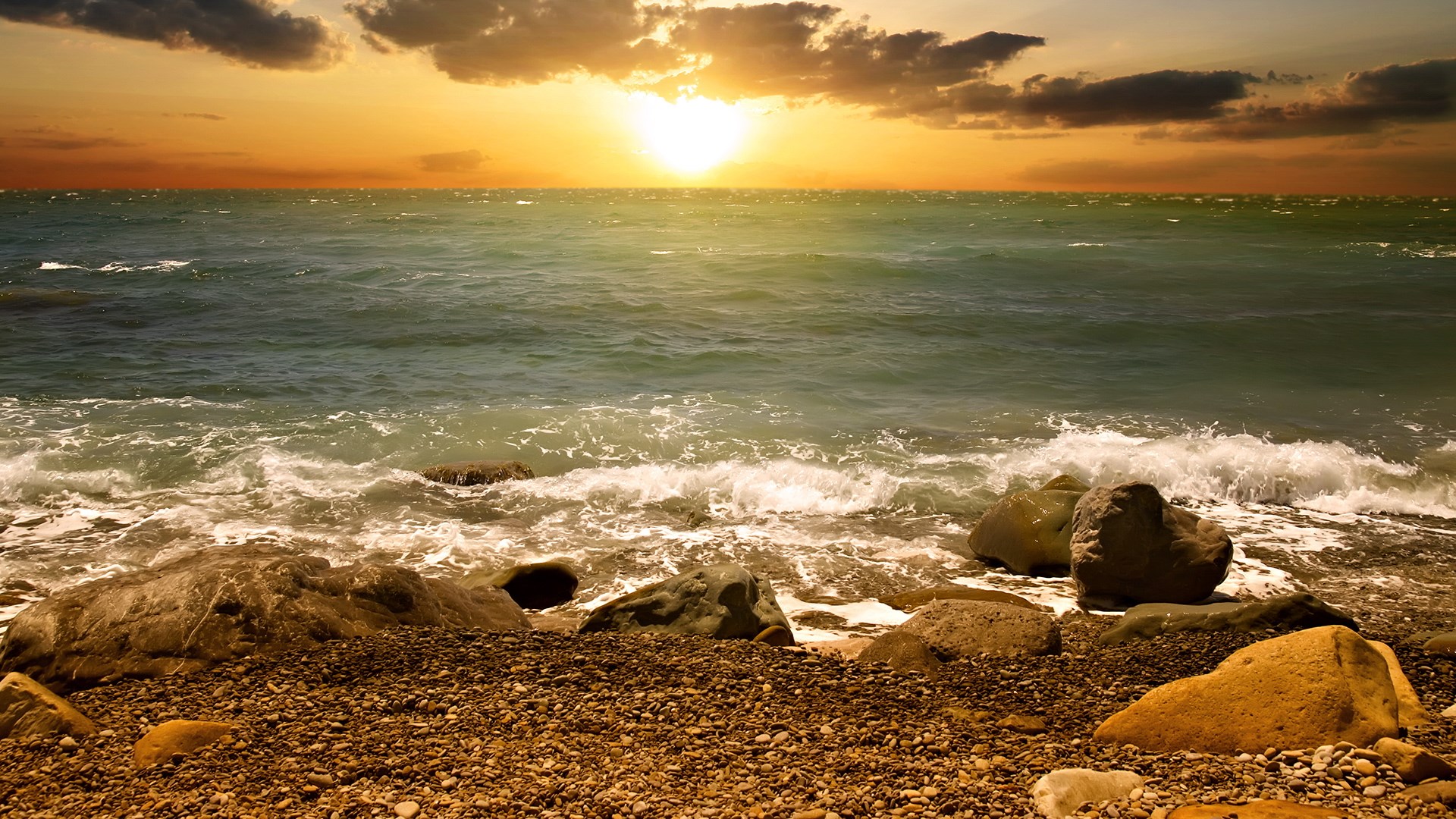 Sunset over the ocean with waves crashing on a rocky shore HD Wallpaper