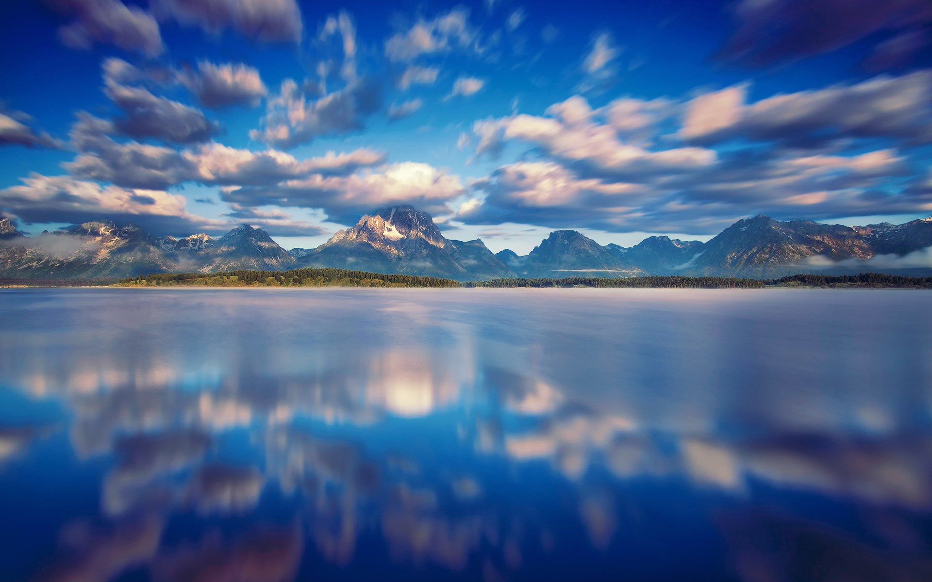 Mountains reflected in a misty lake under a cloudy sky HD Wallpaper