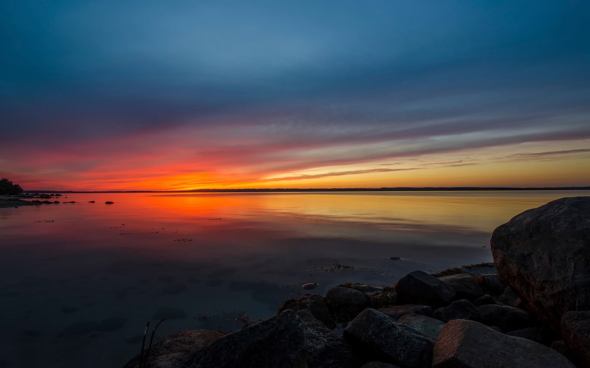 Sunset over a calm body of water with rocks HD Wallpaper