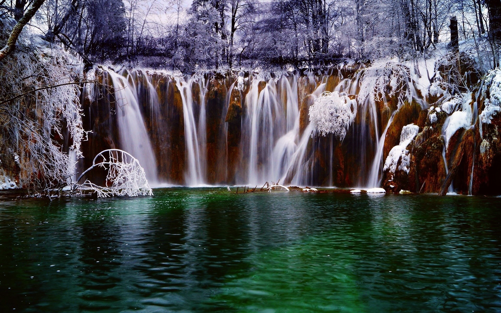 Frozen waterfall with green water and snow-covered trees HD Wallpaper