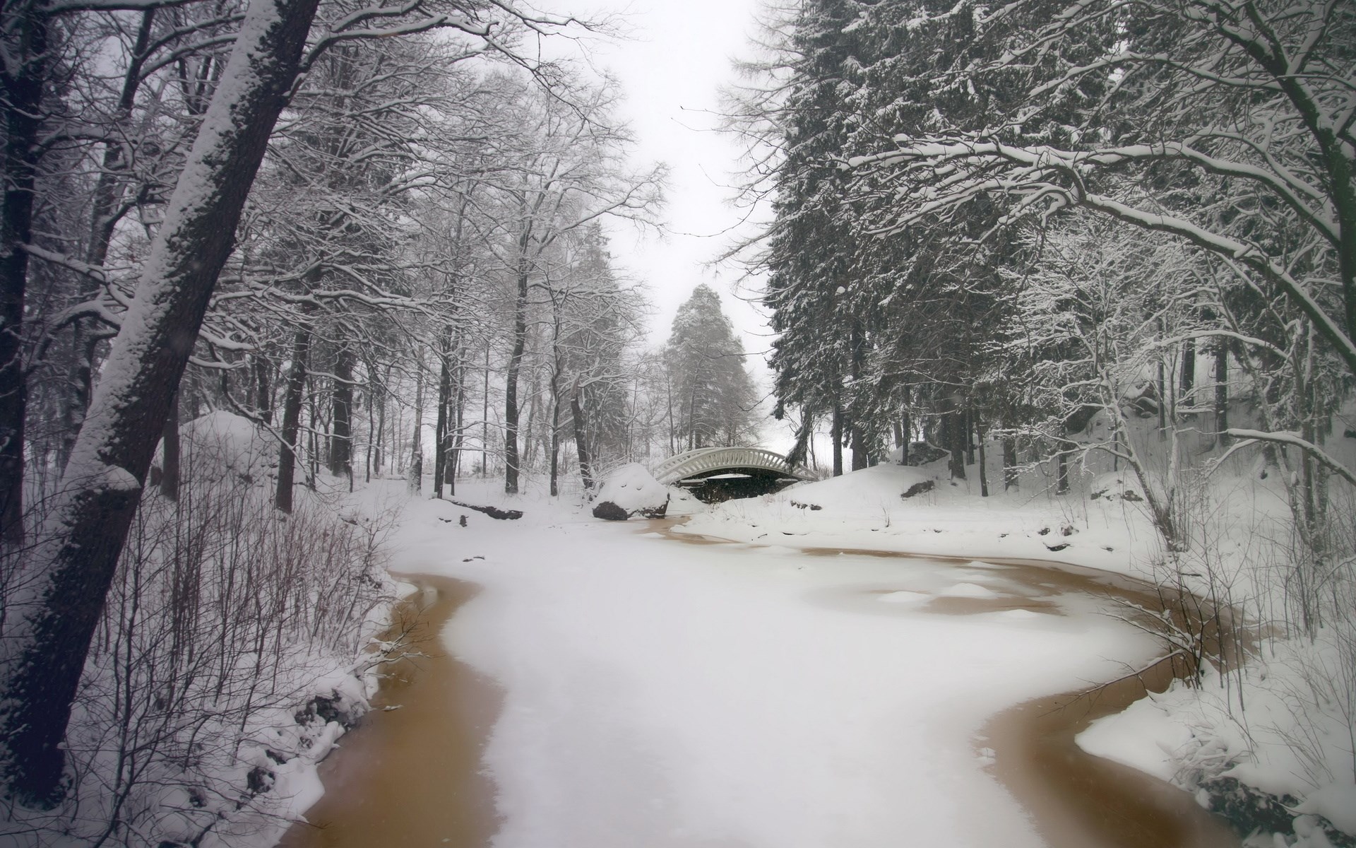 Snowy park with a frozen river and a bridge HD Wallpaper