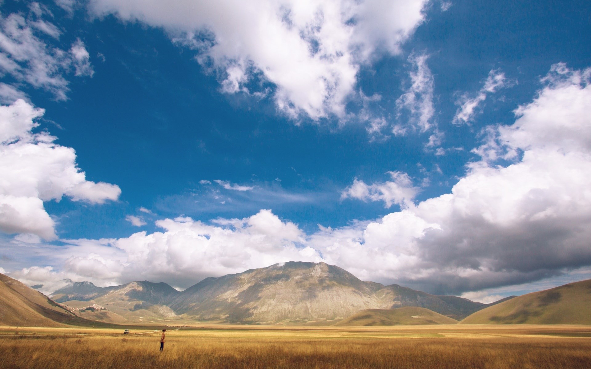 Person standing in a field with mountains and clouds HD Wallpaper