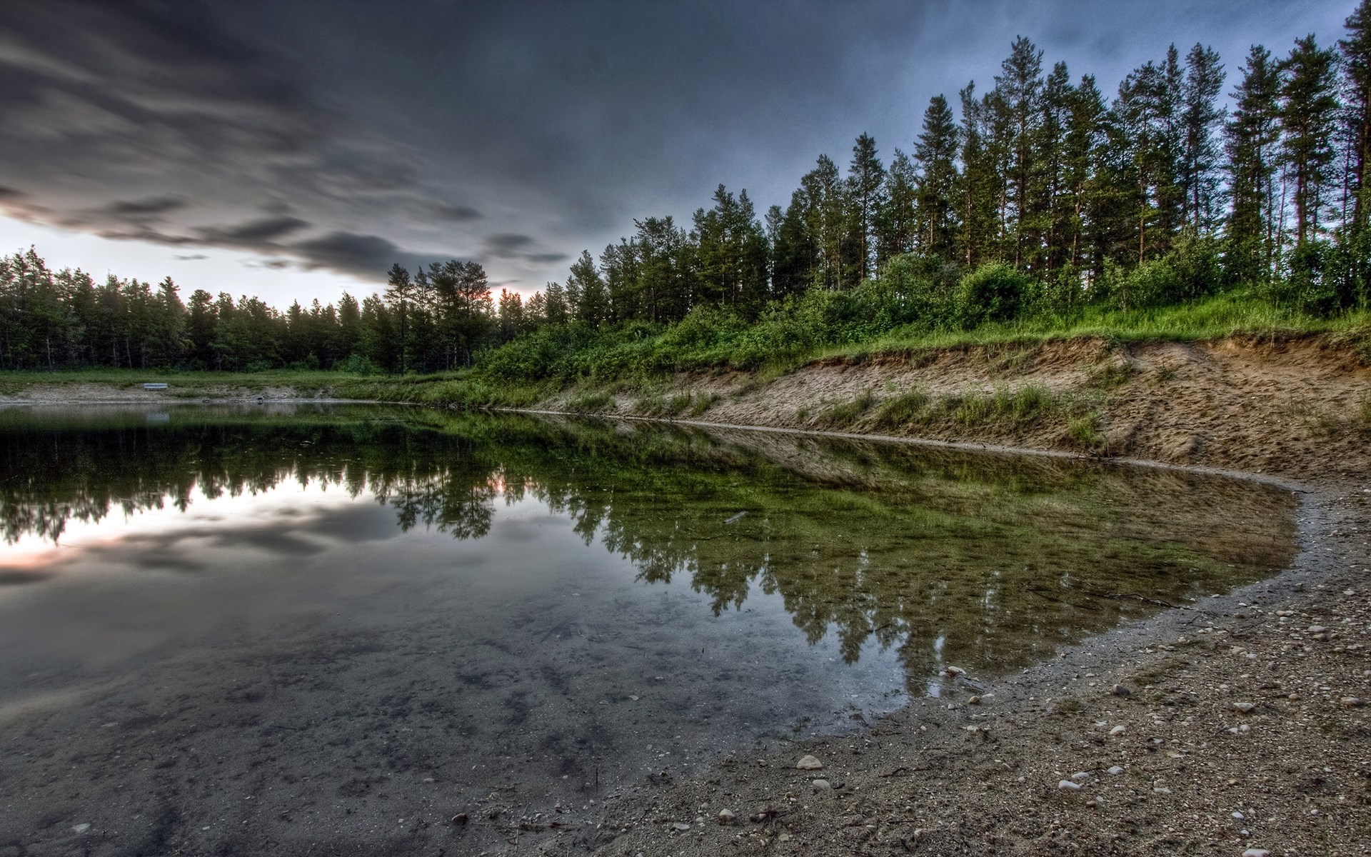 Forest reflecting in a calm lake under a cloudy sky HD Wallpaper