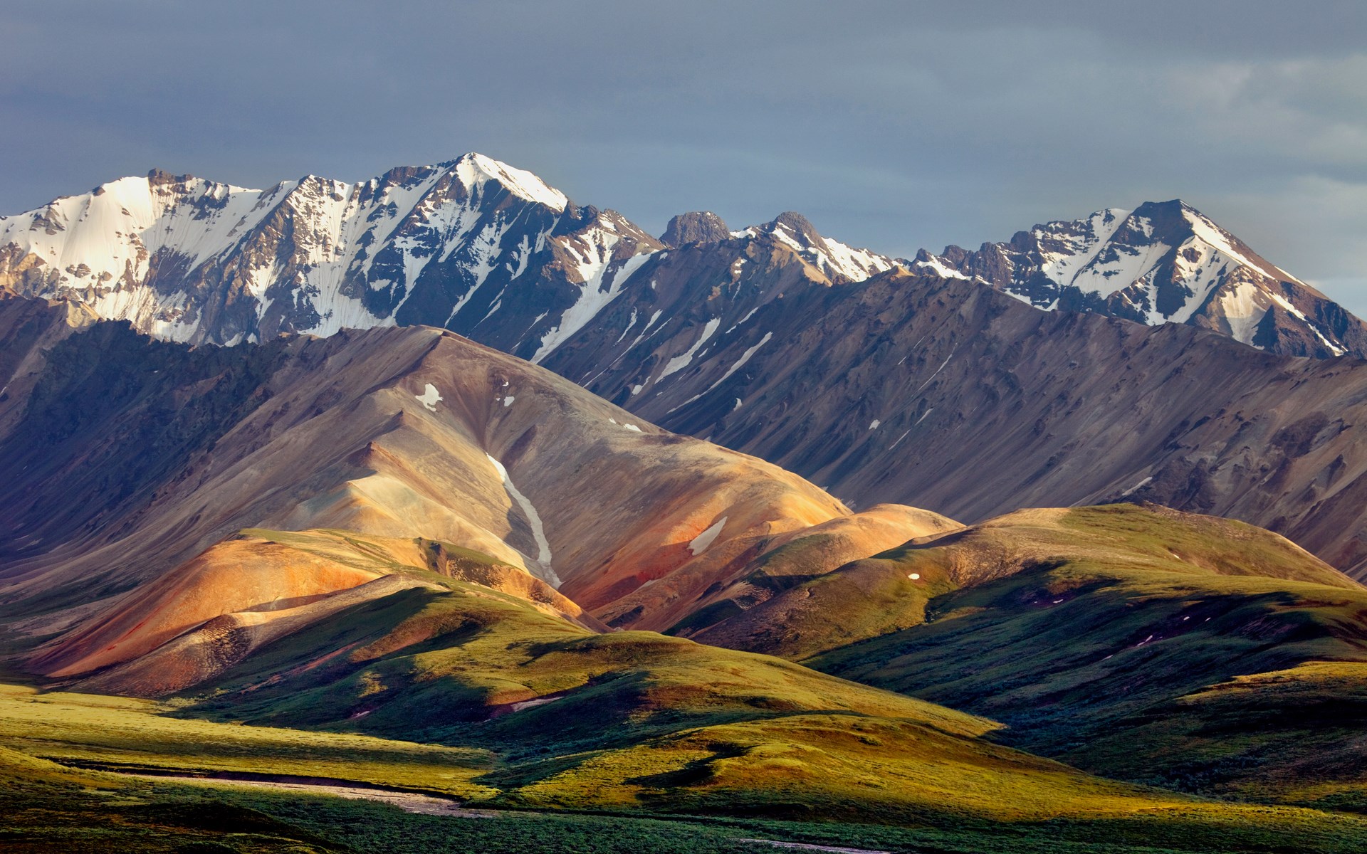 Snow-capped mountains and rolling hills under a cloudy sky HD Wallpaper
