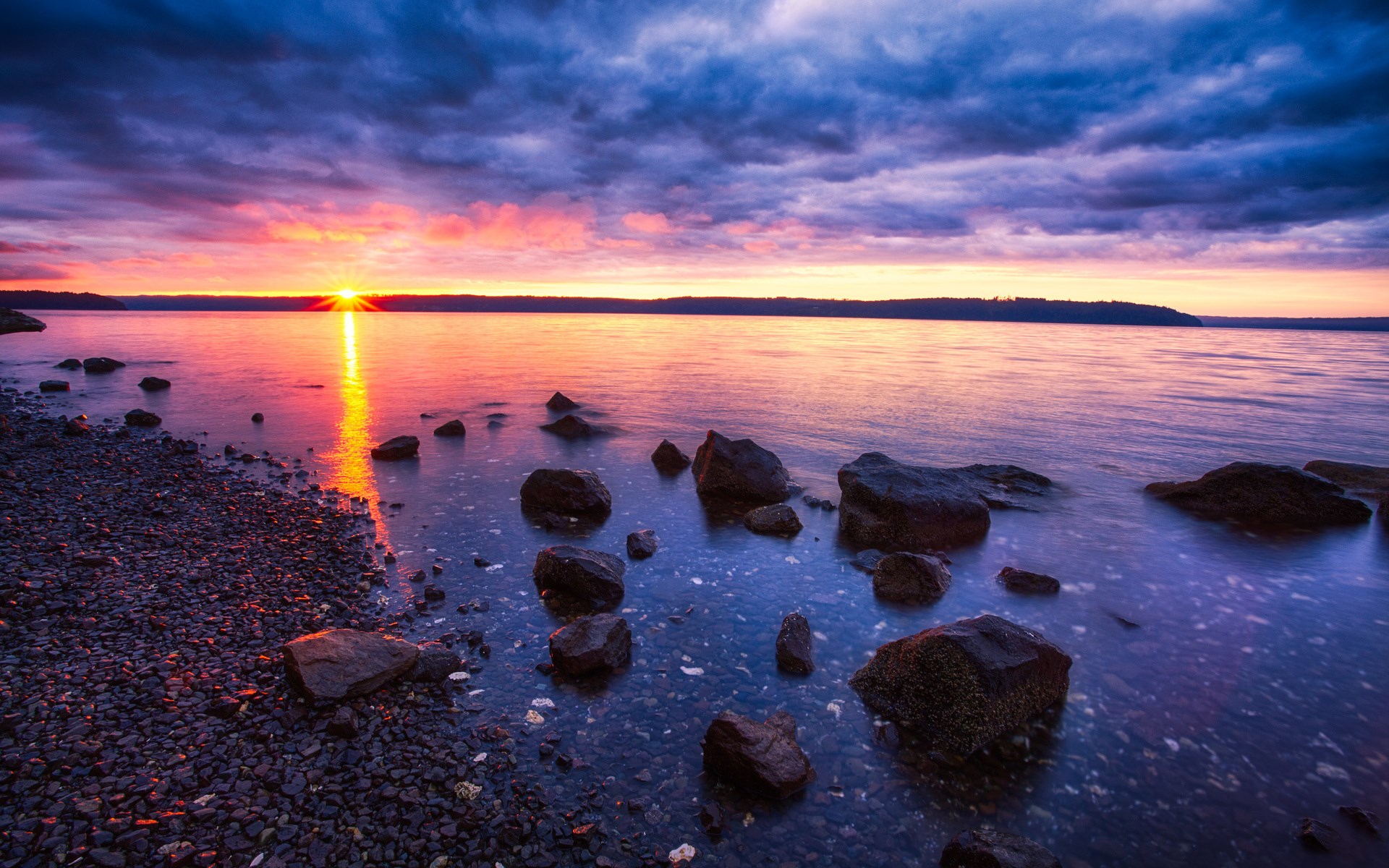 Sunset over a rocky shore with calm water HD Wallpaper