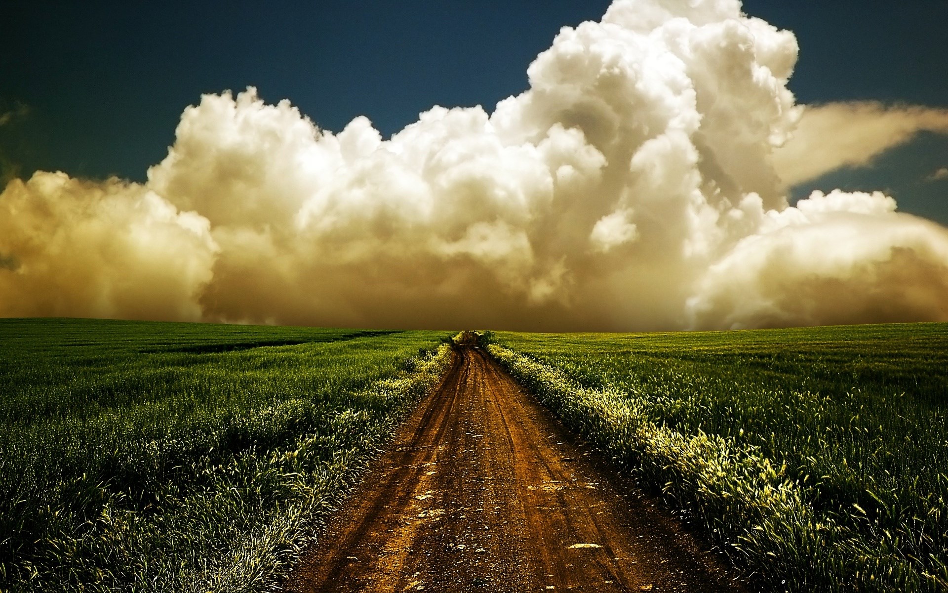 Dirt road through a green field under dramatic clouds HD Wallpaper