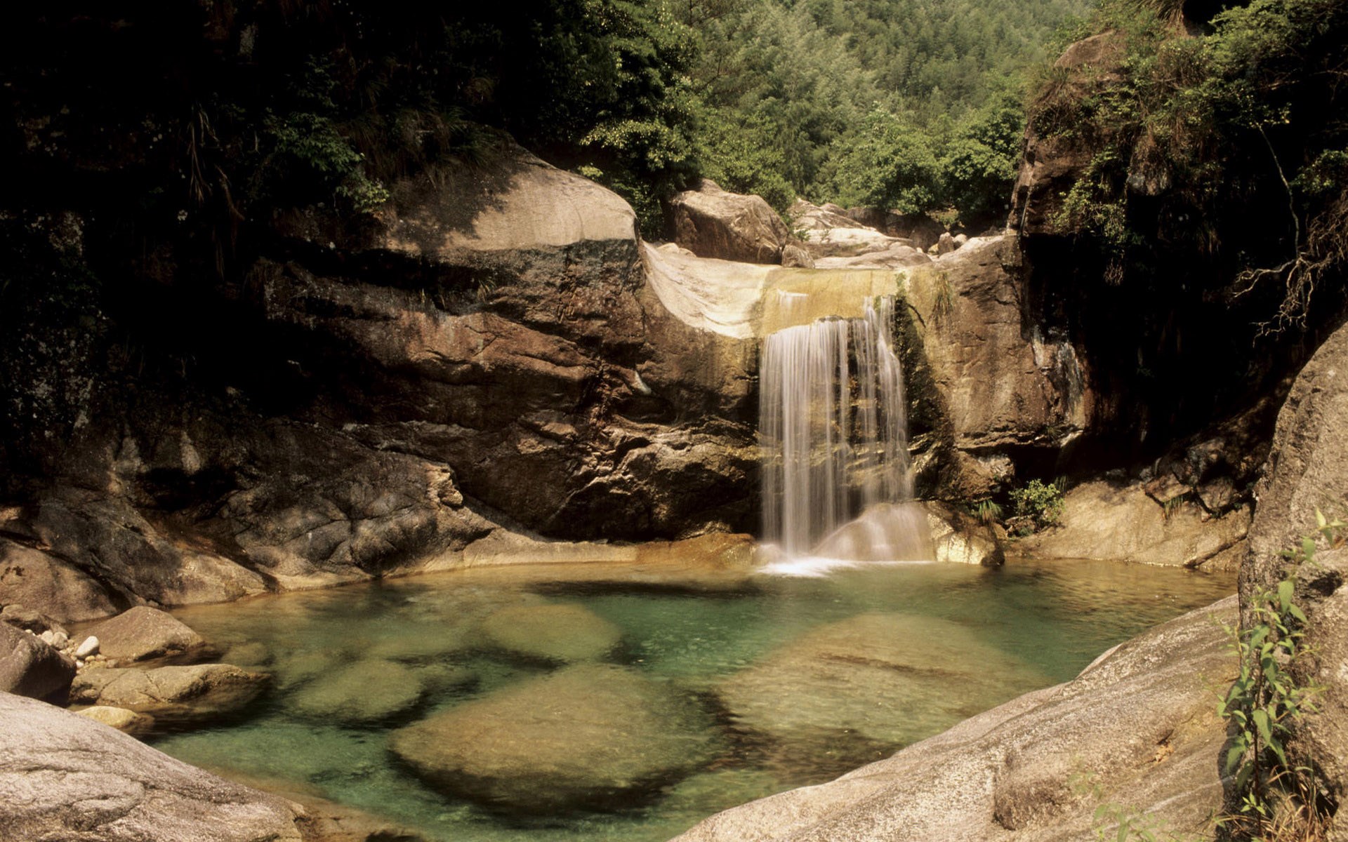 Waterfall cascading into a clear pool in a rocky forest HD Wallpaper