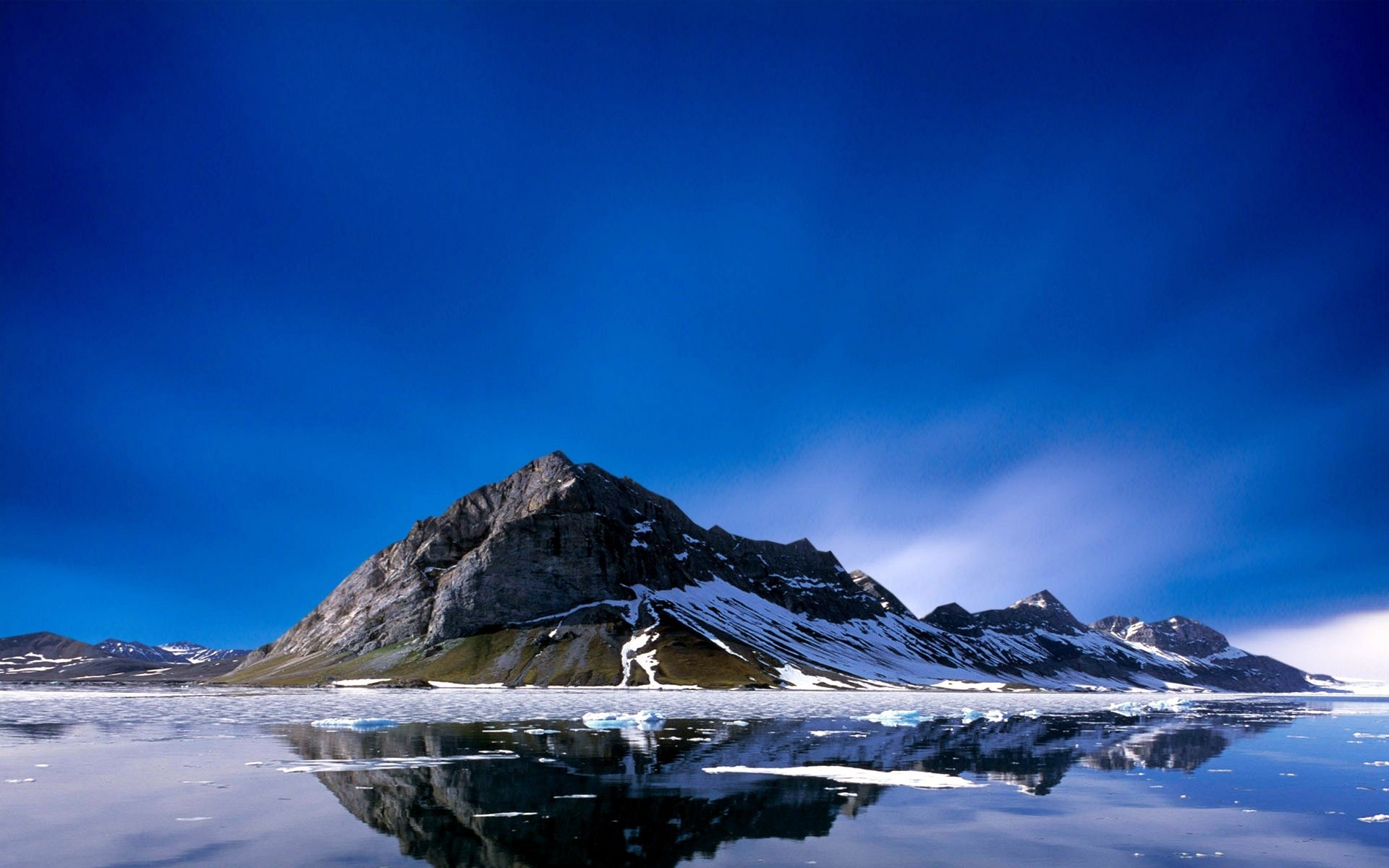 Snow-capped mountains reflected in icy water under a blue sky HD Wallpaper