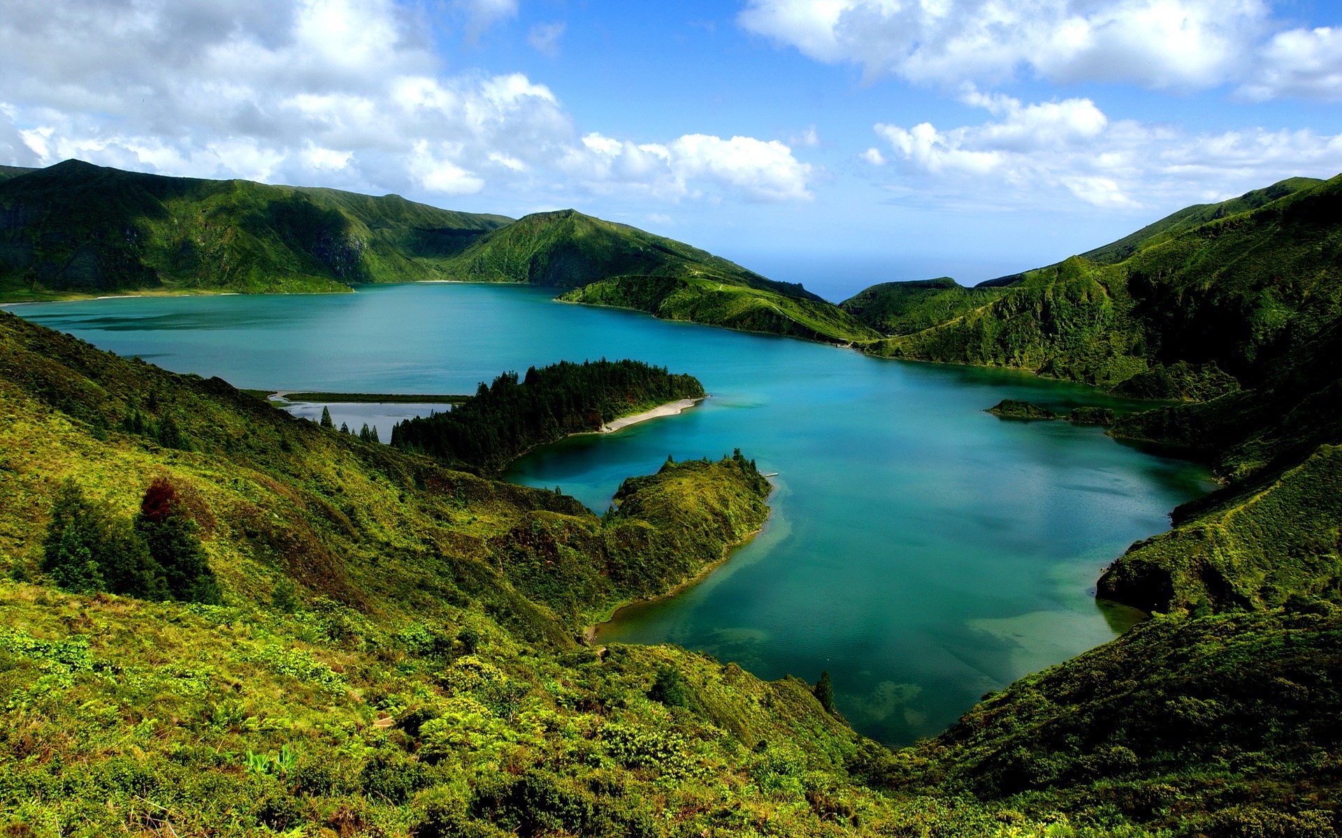 Green volcanic crater lake with islands under blue sky HD Wallpaper