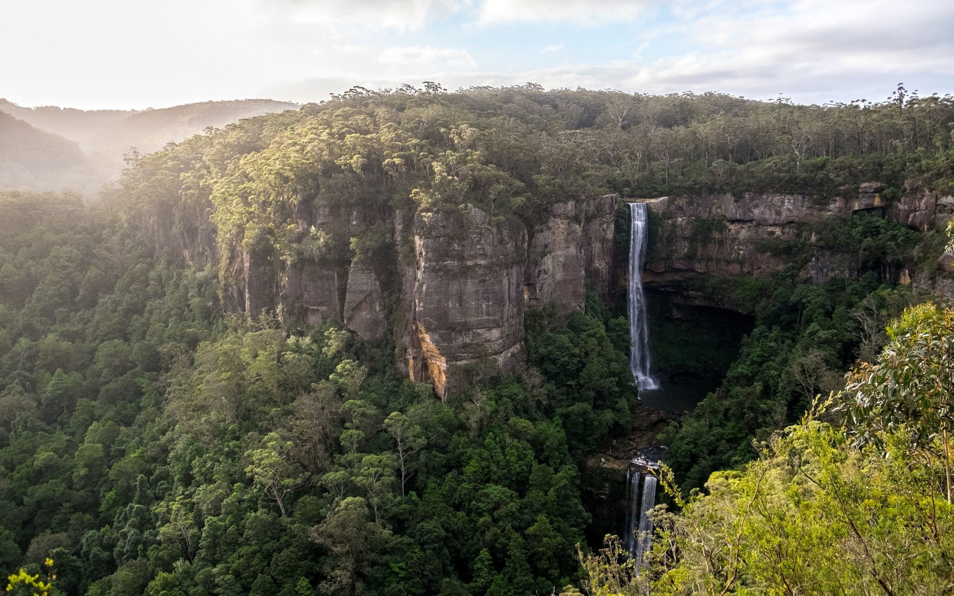 Waterfall cascading down a cliff face in a forest HD Wallpaper