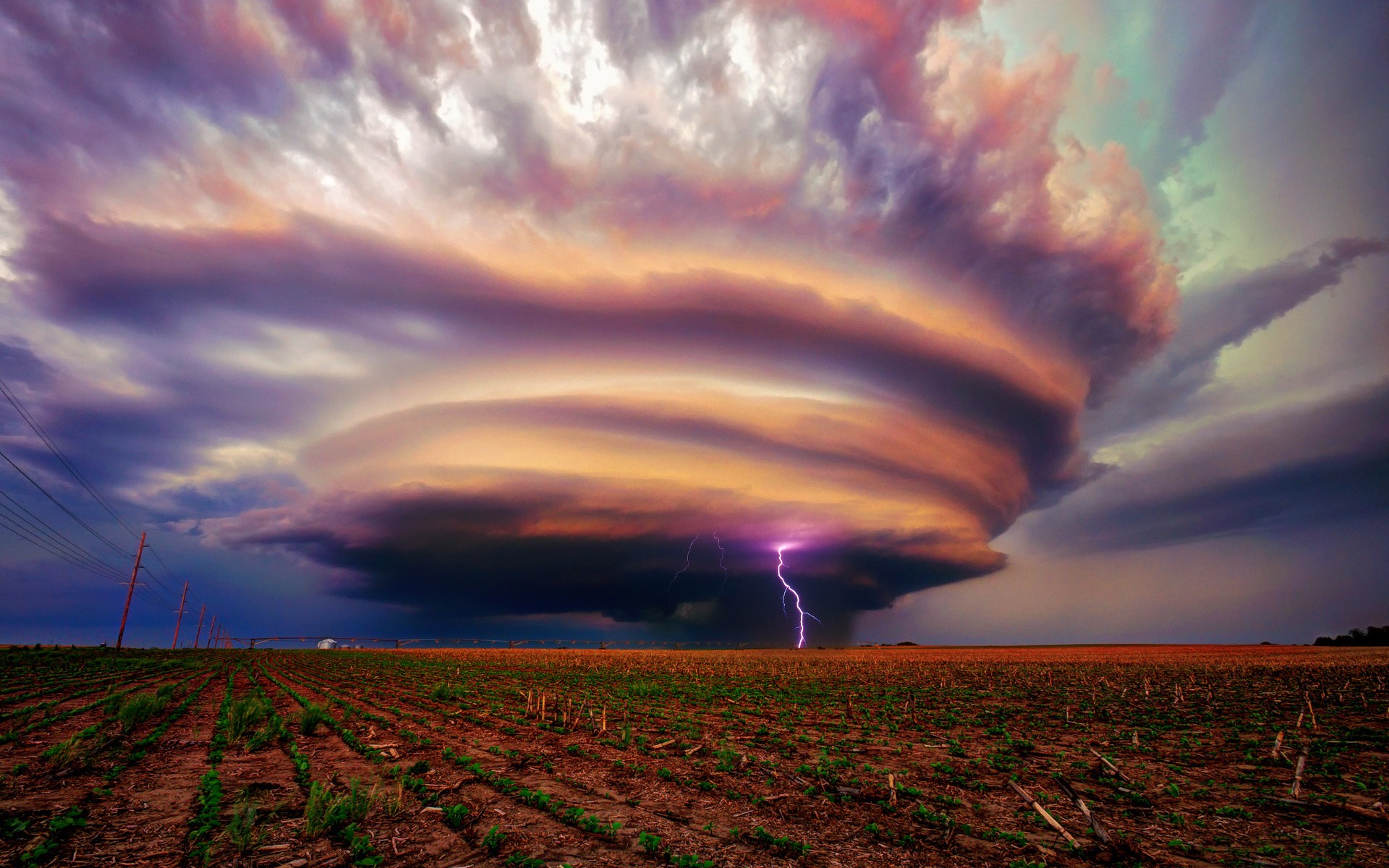 Lightning strikes a supercell thunderstorm over a farm field HD Wallpaper