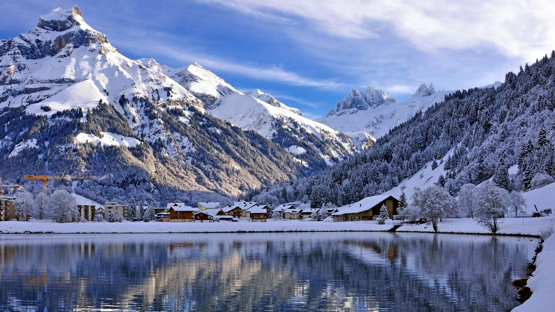 Snowy mountains reflected in a lake with a village HD Wallpaper
