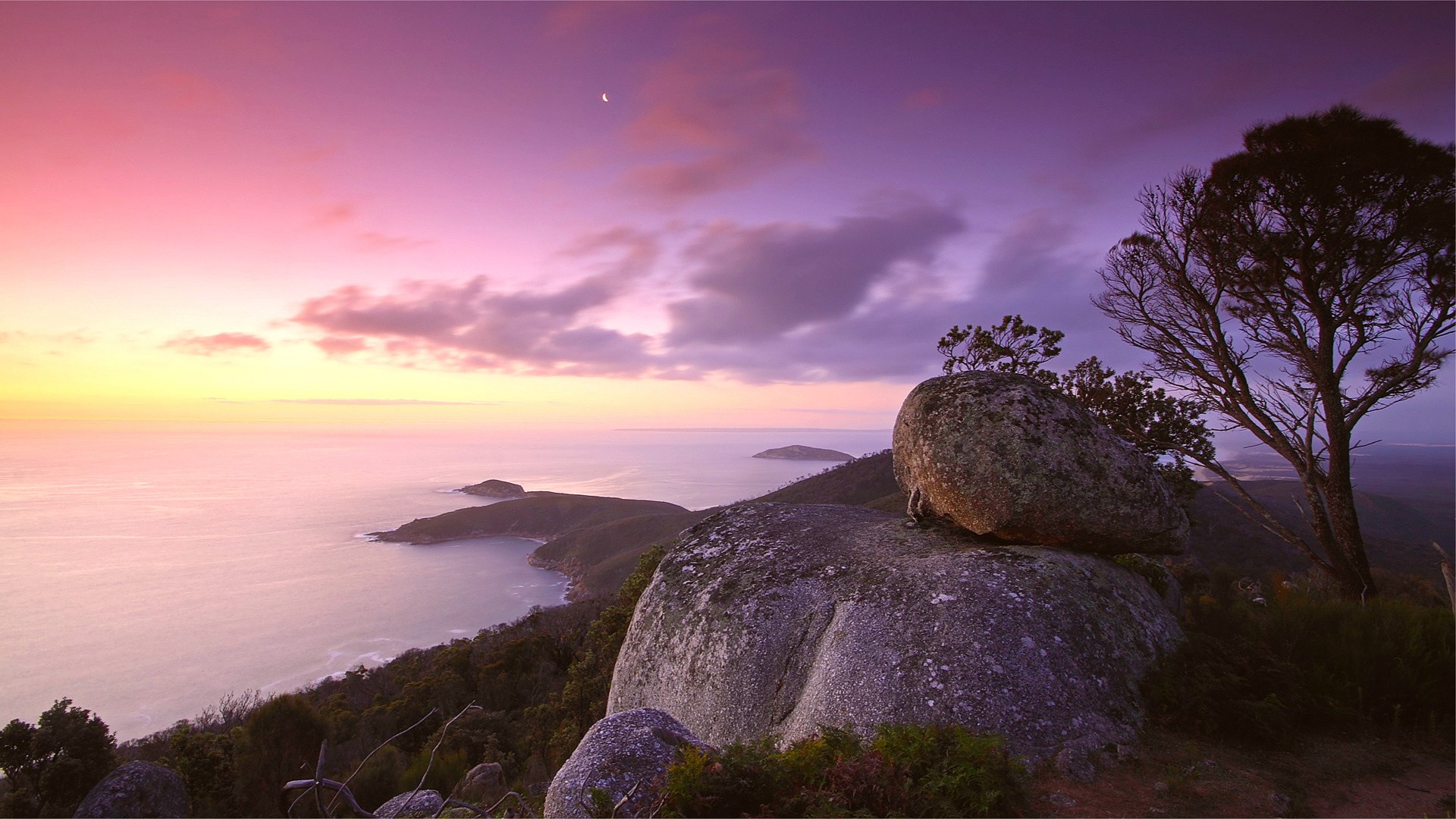 Sunset over a rocky coastline with a crescent moon HD Wallpaper