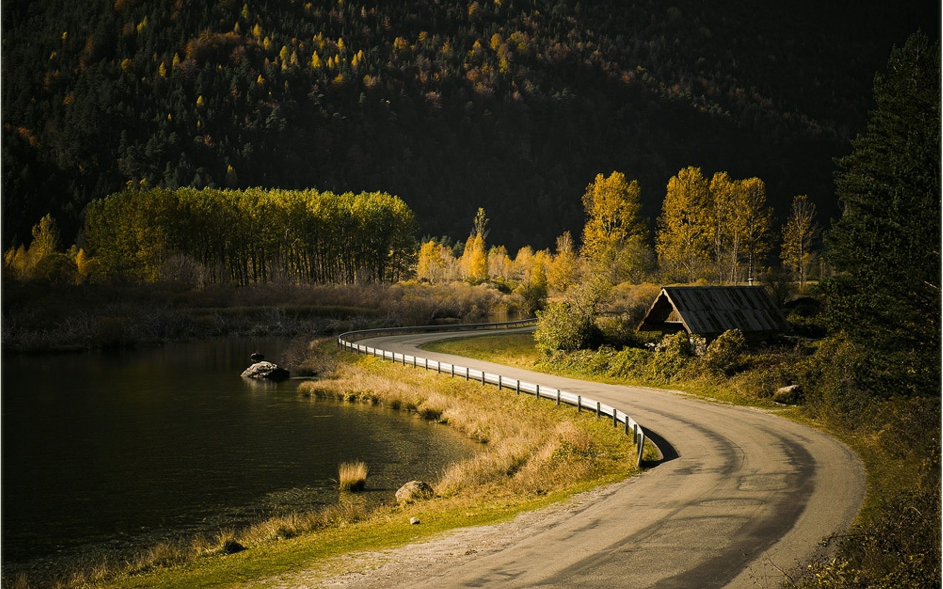 Curving road by a lake with autumn trees and a small cabin HD Wallpaper