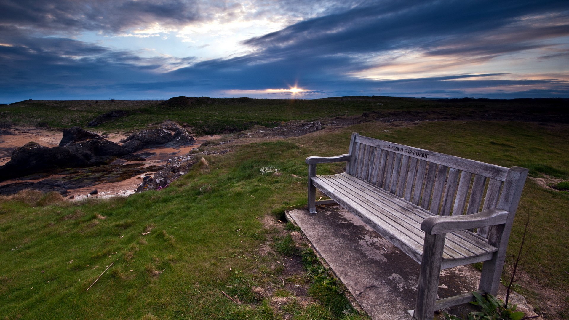 Wooden bench overlooking a coastal landscape at sunset HD Wallpaper