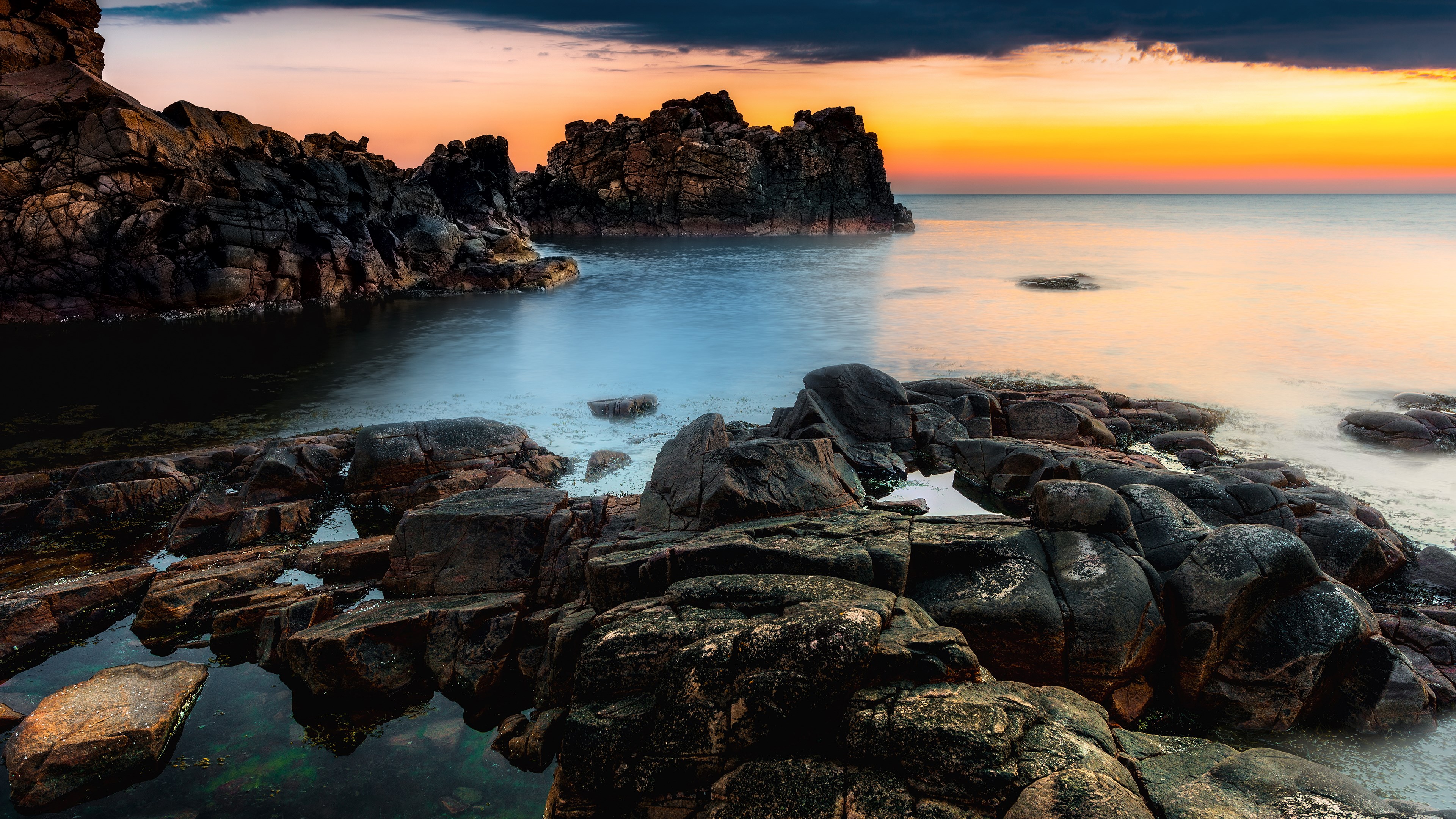 Rocky coastline at sunset with calm ocean HD Wallpaper