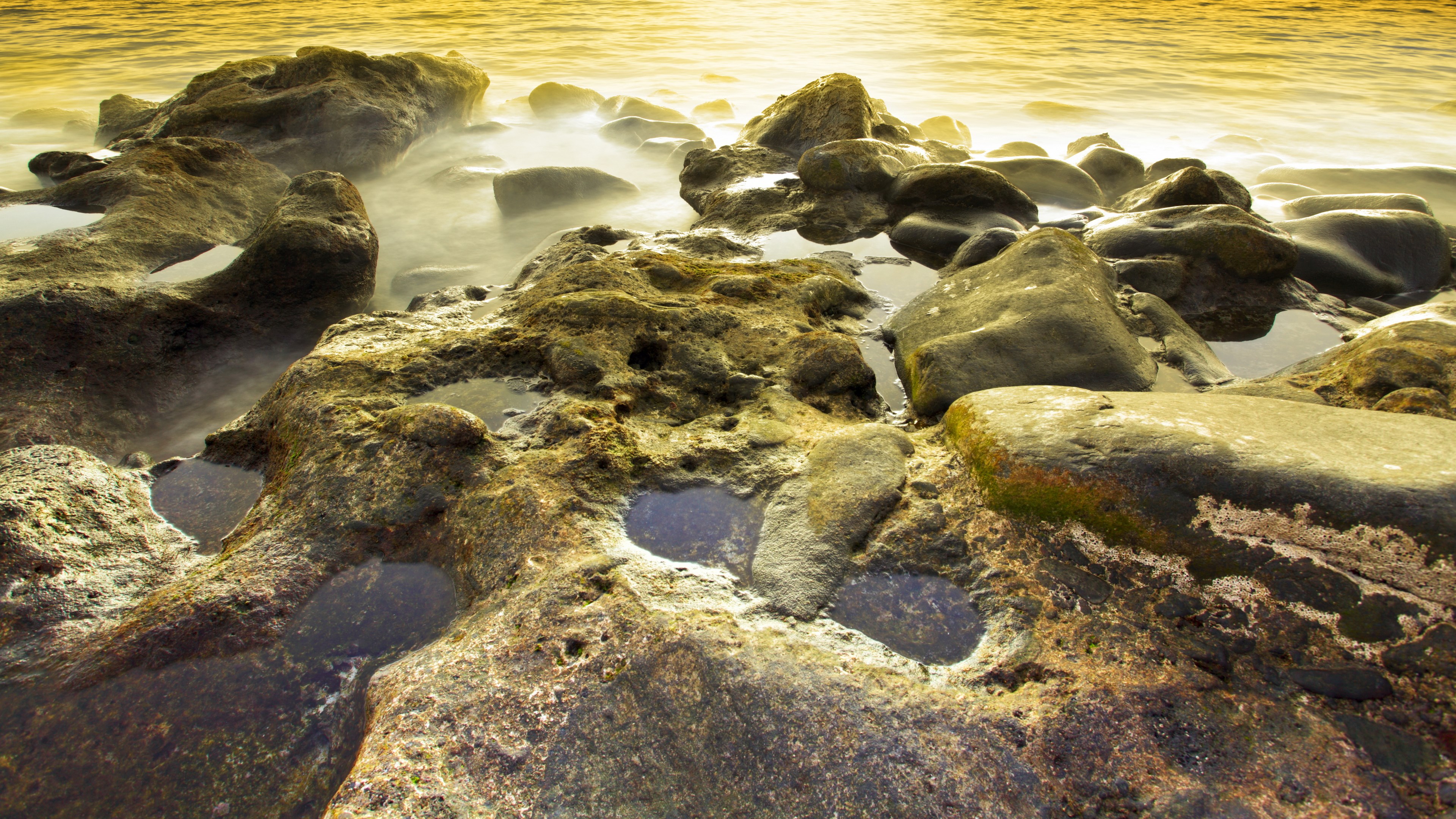 Rocky shoreline with golden water and tide pools HD Wallpaper