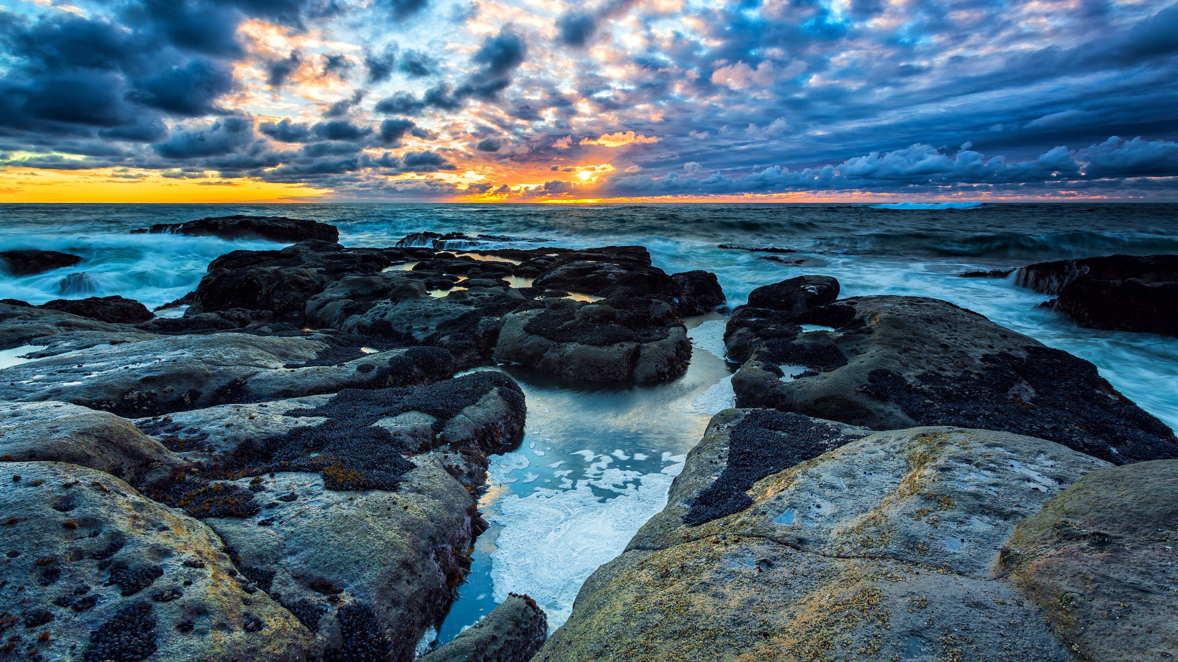 Sunset over rocky coastline with crashing waves HD Wallpaper