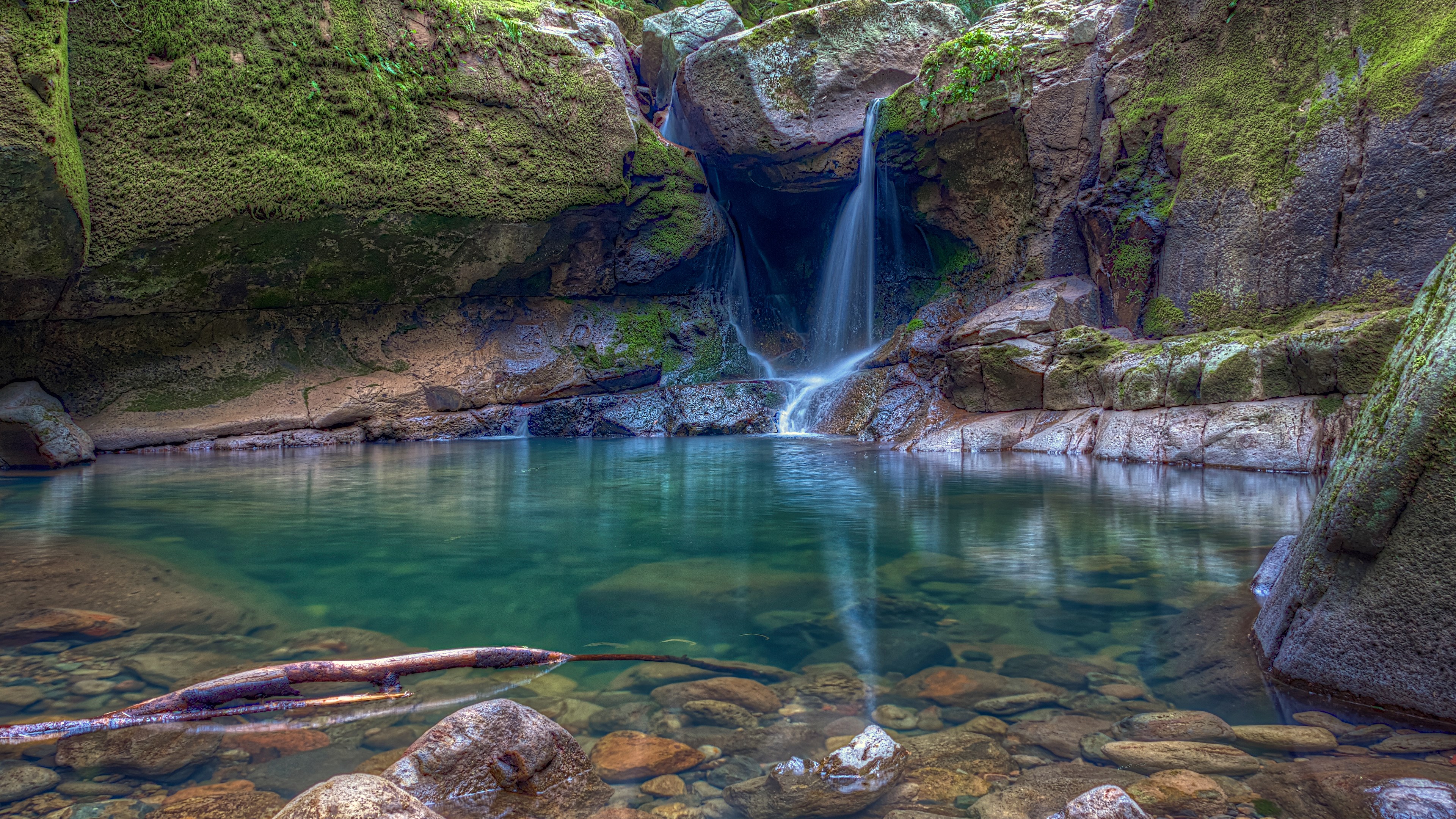 Waterfall cascading into a clear pool surrounded by mossy rocks HD Wallpaper