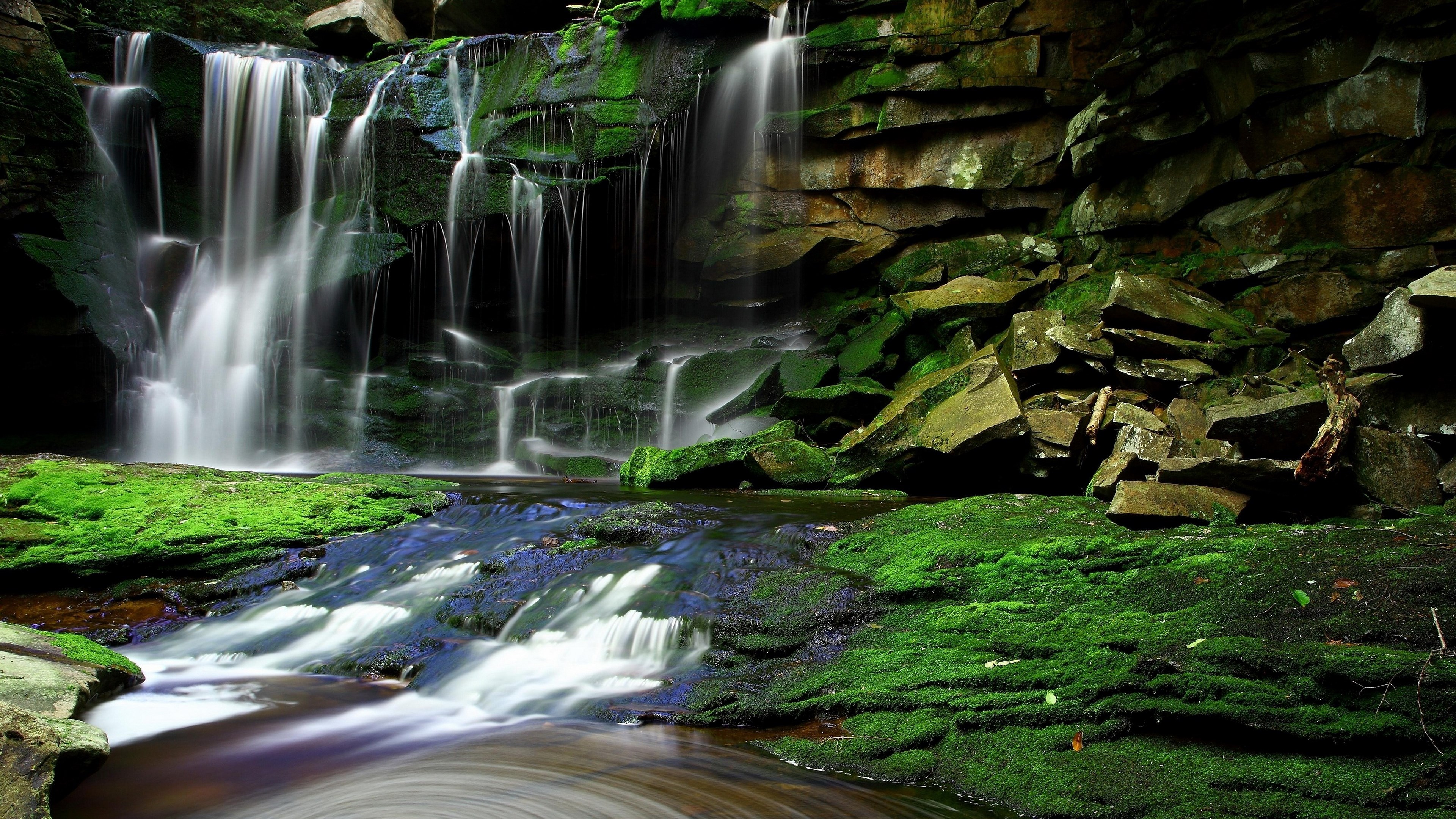 Waterfall cascading over moss-covered rocks into a stream HD Wallpaper