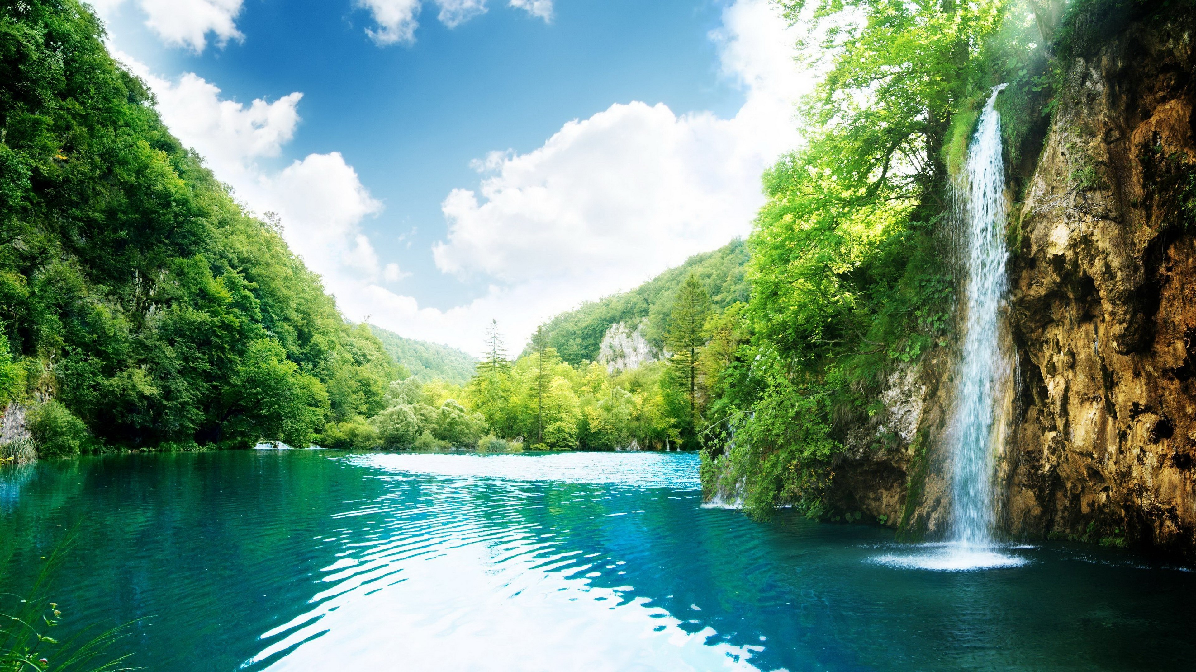 Waterfall cascading into a turquoise lake surrounded by green forest HD Wallpaper