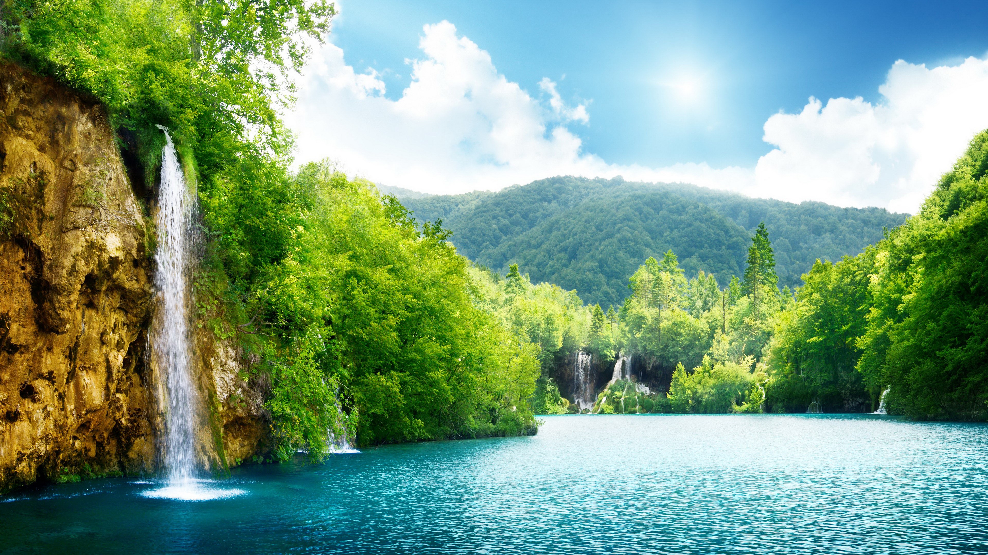 Waterfall cascading into a turquoise lake surrounded by green forest HD Wallpaper