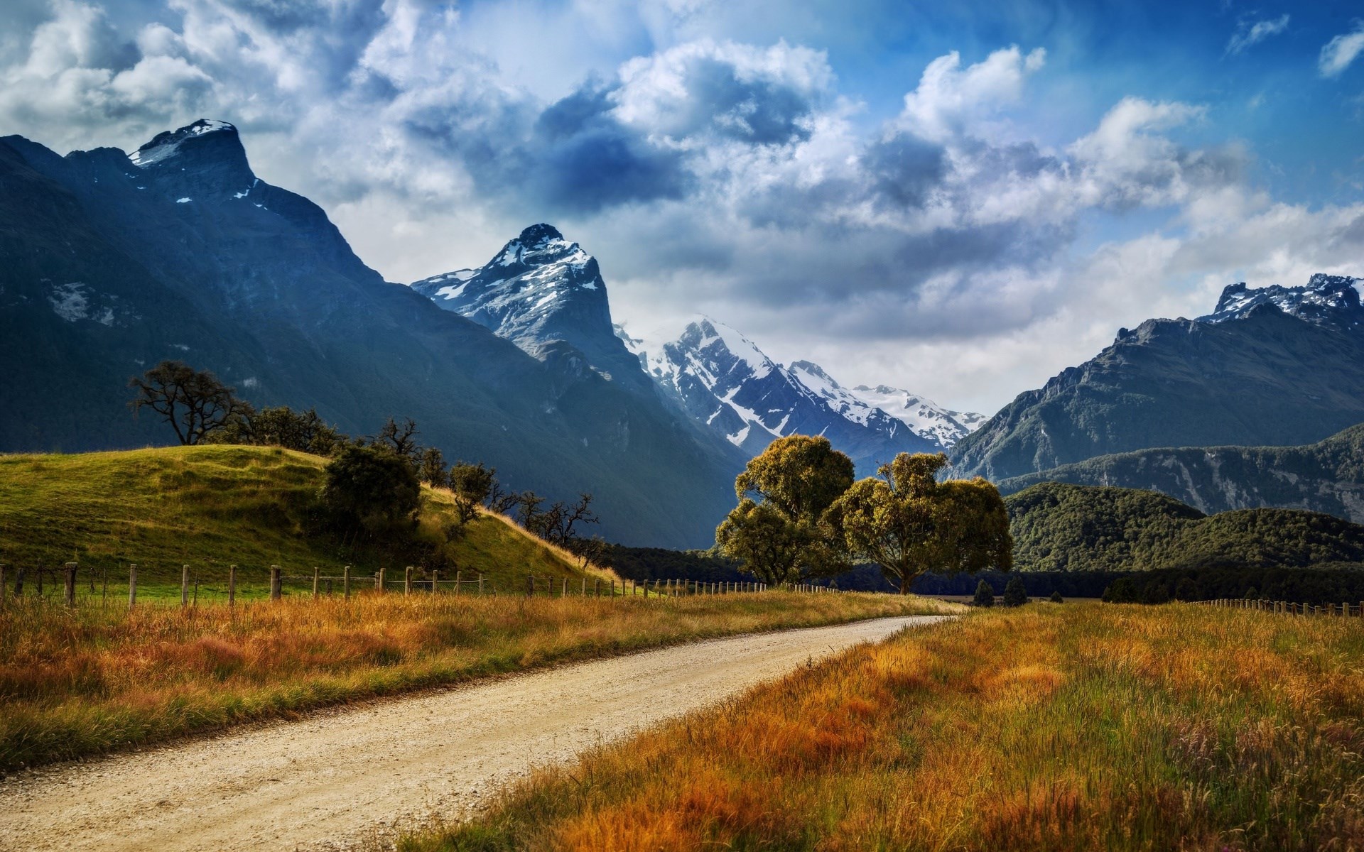 Dirt road through a grassy field with mountains HD Wallpaper