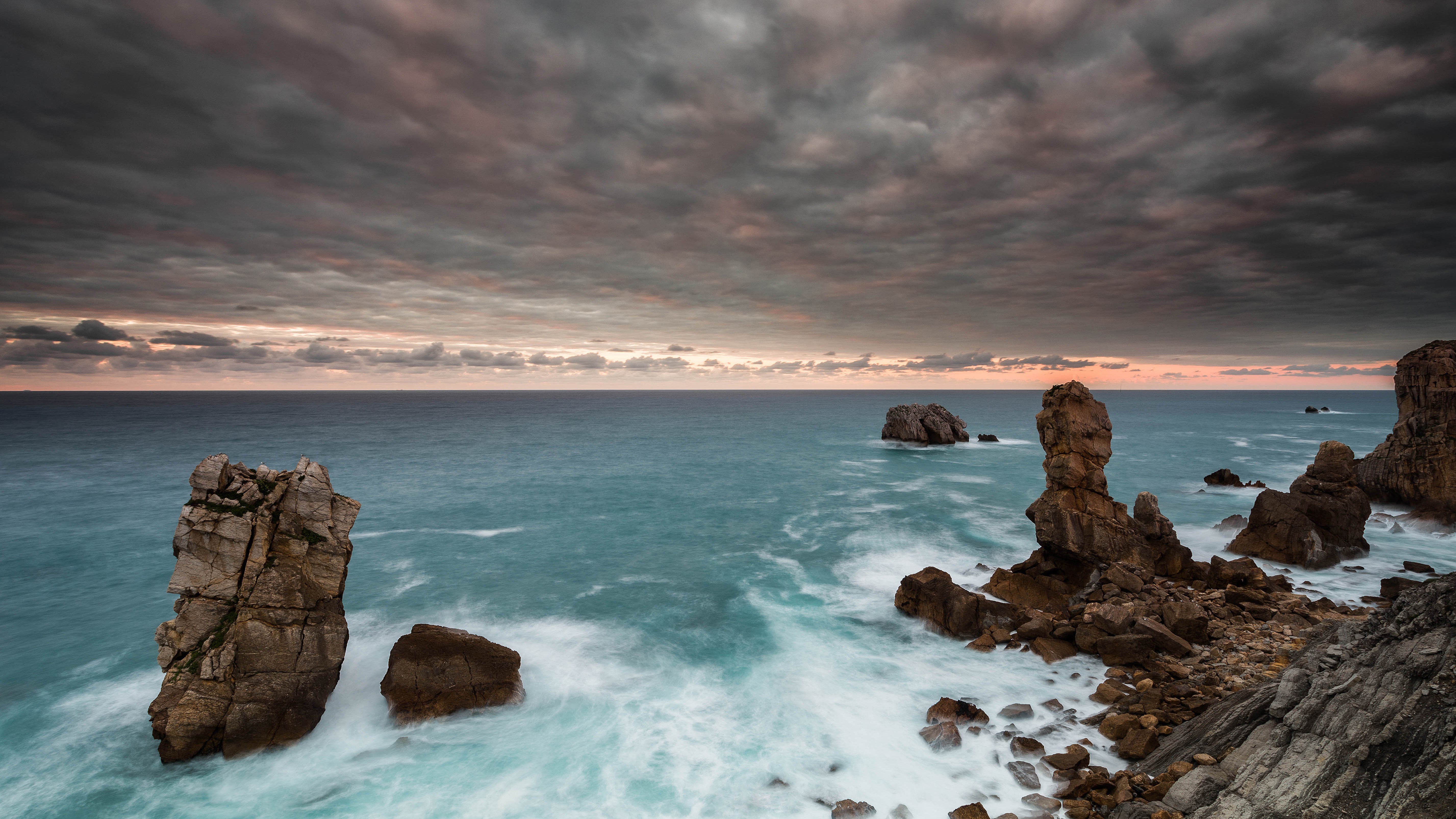 Rocky coast with waves crashing under cloudy sky HD Wallpaper