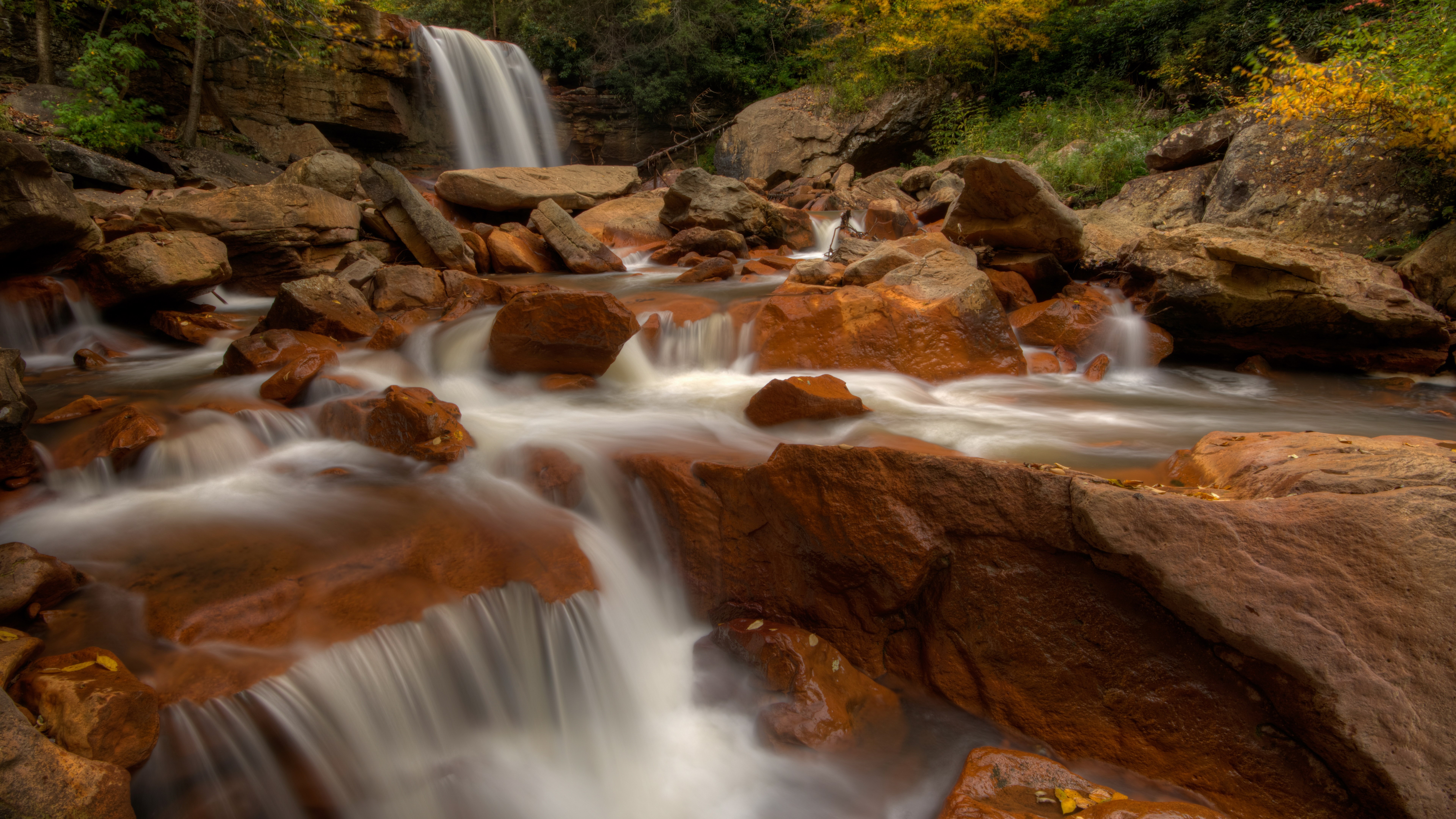 Waterfall flowing over reddish-brown rocks in a forest HD Wallpaper