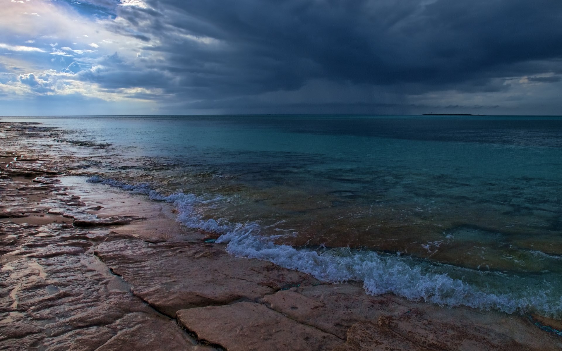 Rocky shoreline with turquoise ocean and stormy clouds HD Wallpaper