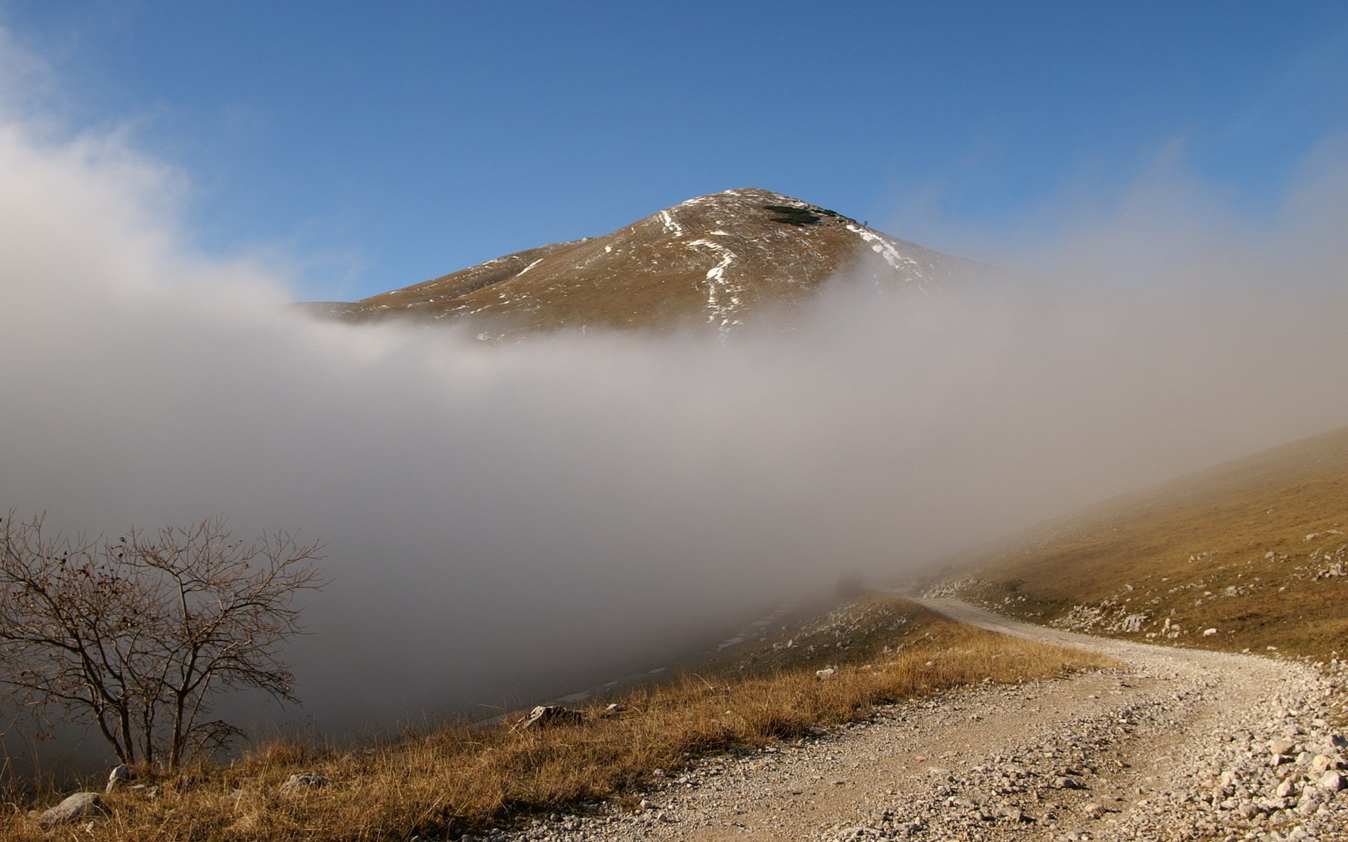 Mountain peak emerging from clouds with a dirt road HD Wallpaper