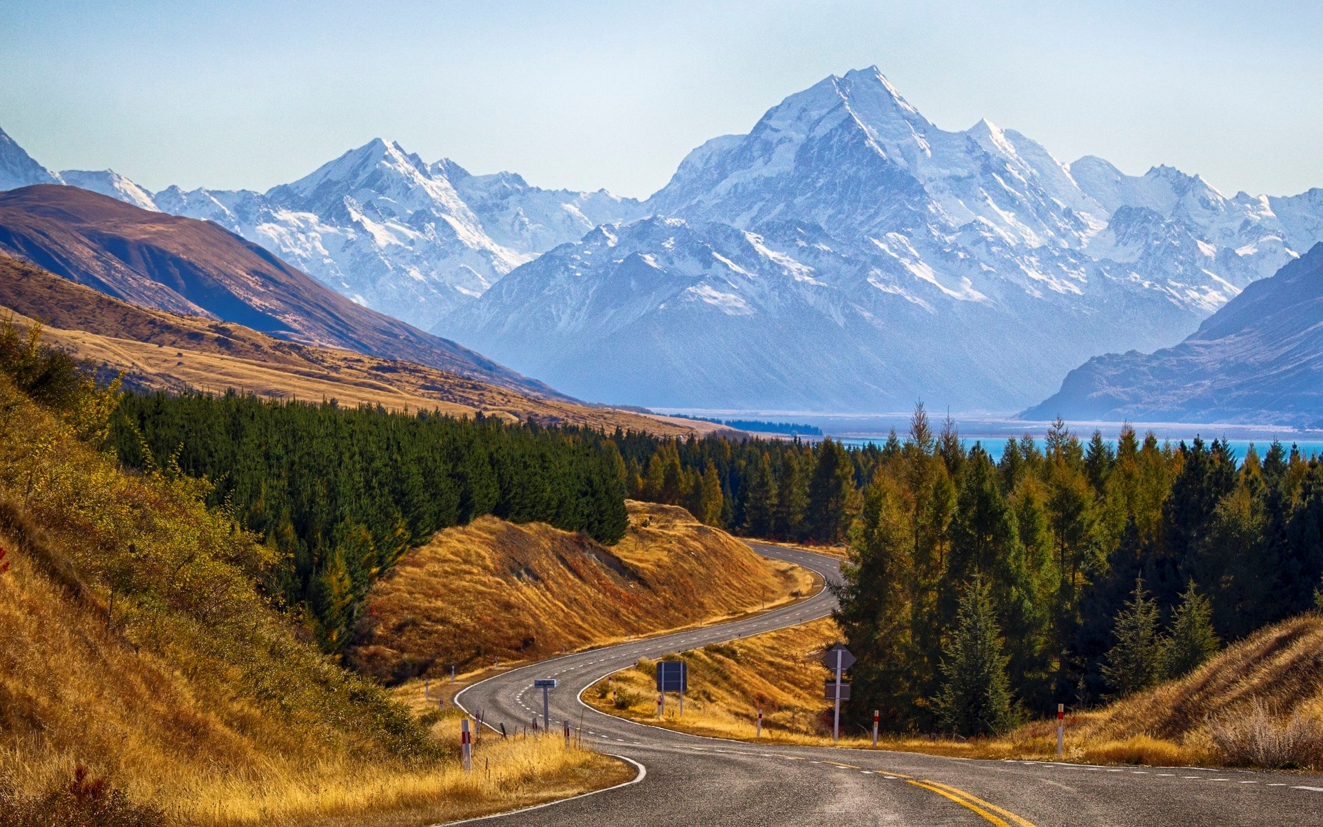 Winding road through autumn landscape towards snow-capped mountains HD Wallpaper