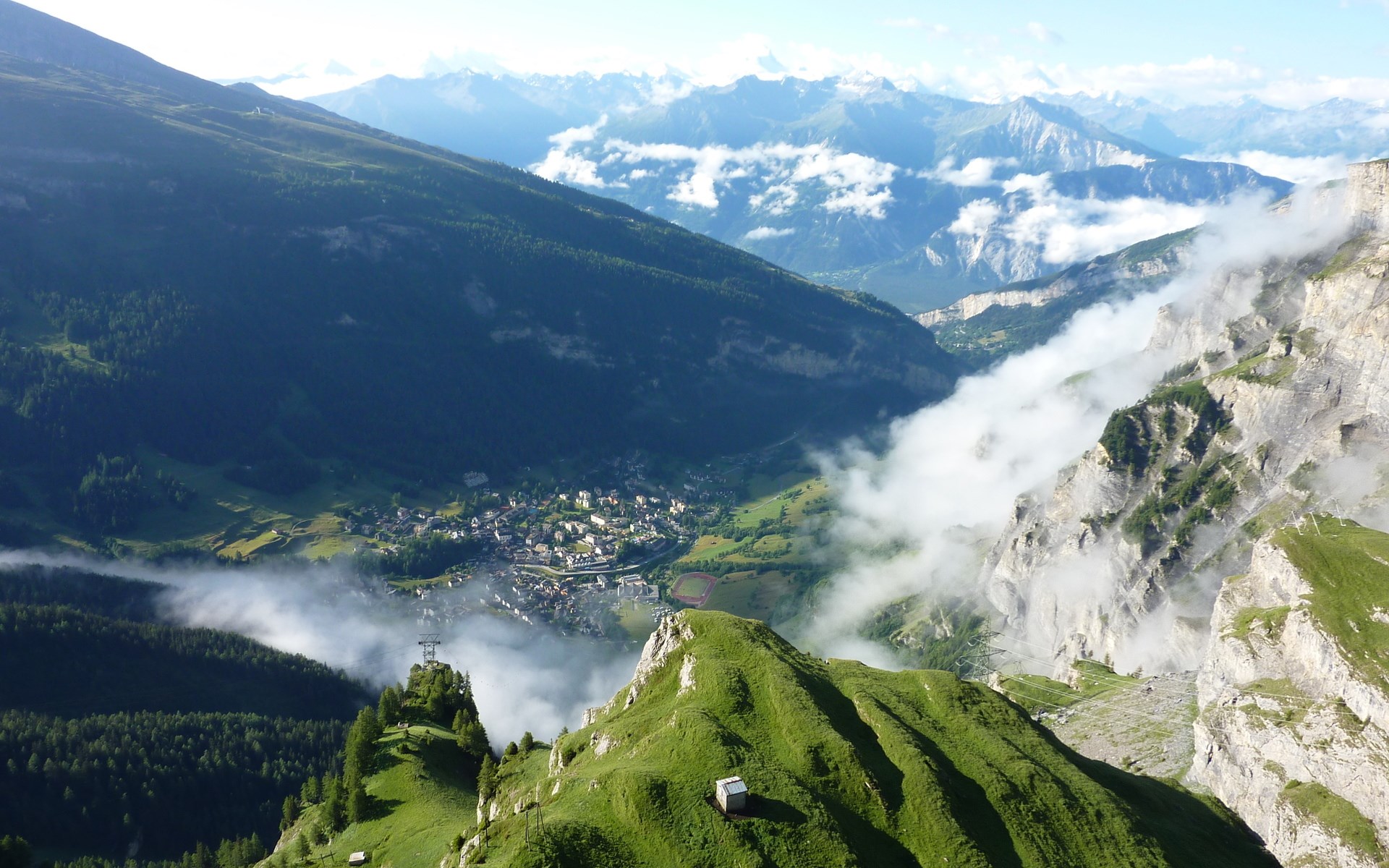 Mountain village nestled in a valley with clouds HD Wallpaper