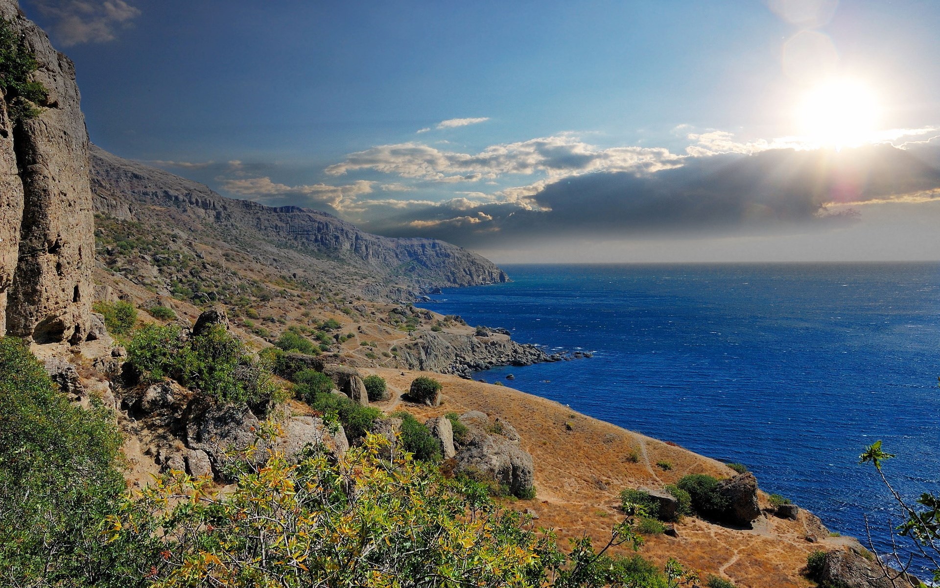 Rocky coastline with blue ocean and bright sun HD Wallpaper